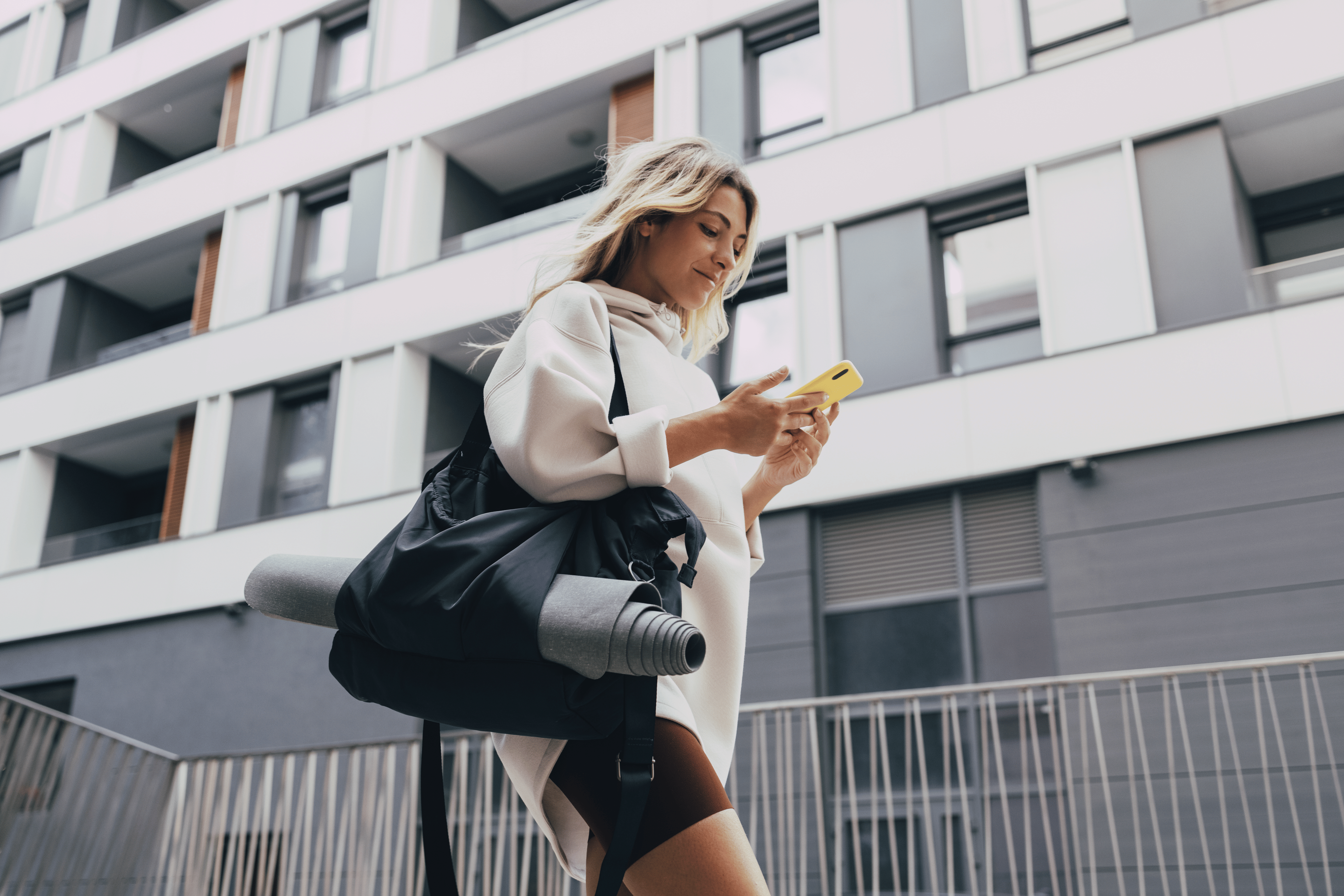 Woman carries gym bag with yoga mat while using a mobile phone