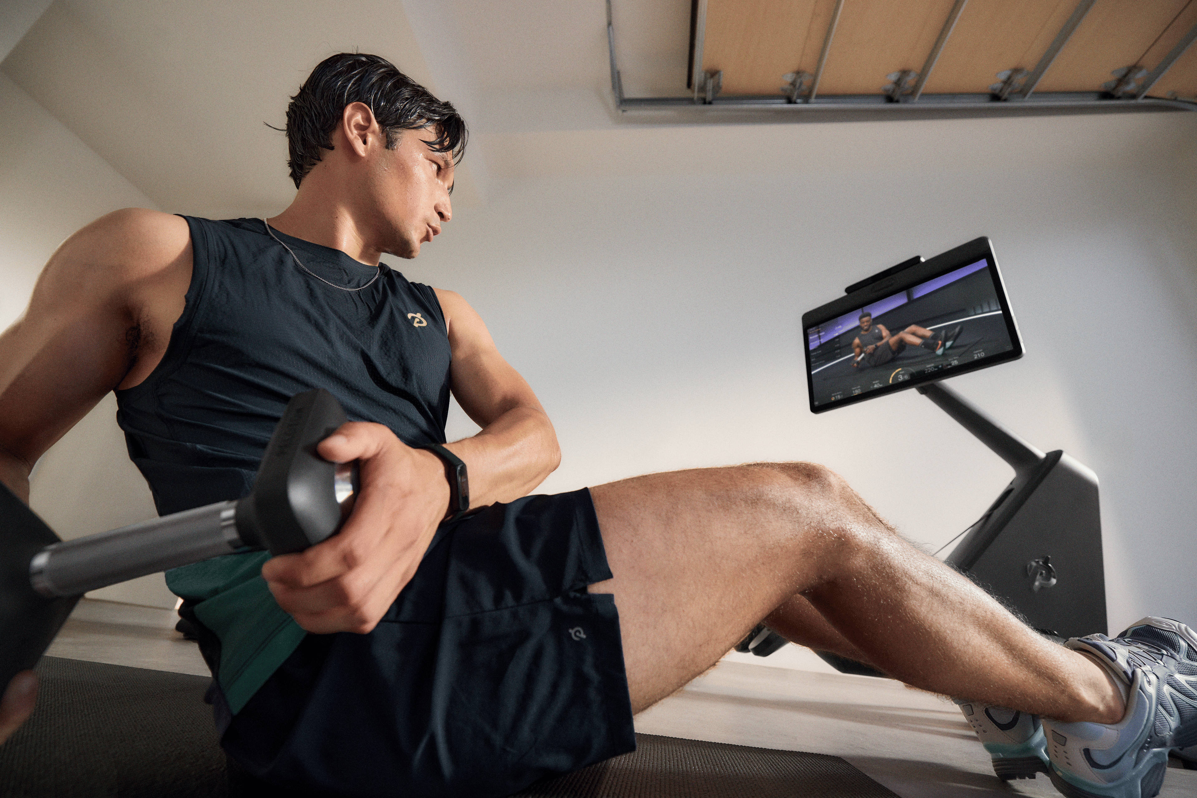 Man working out in his garage gym with the Peloton Cross Training Row+ using the strength exercise form feedback feature.