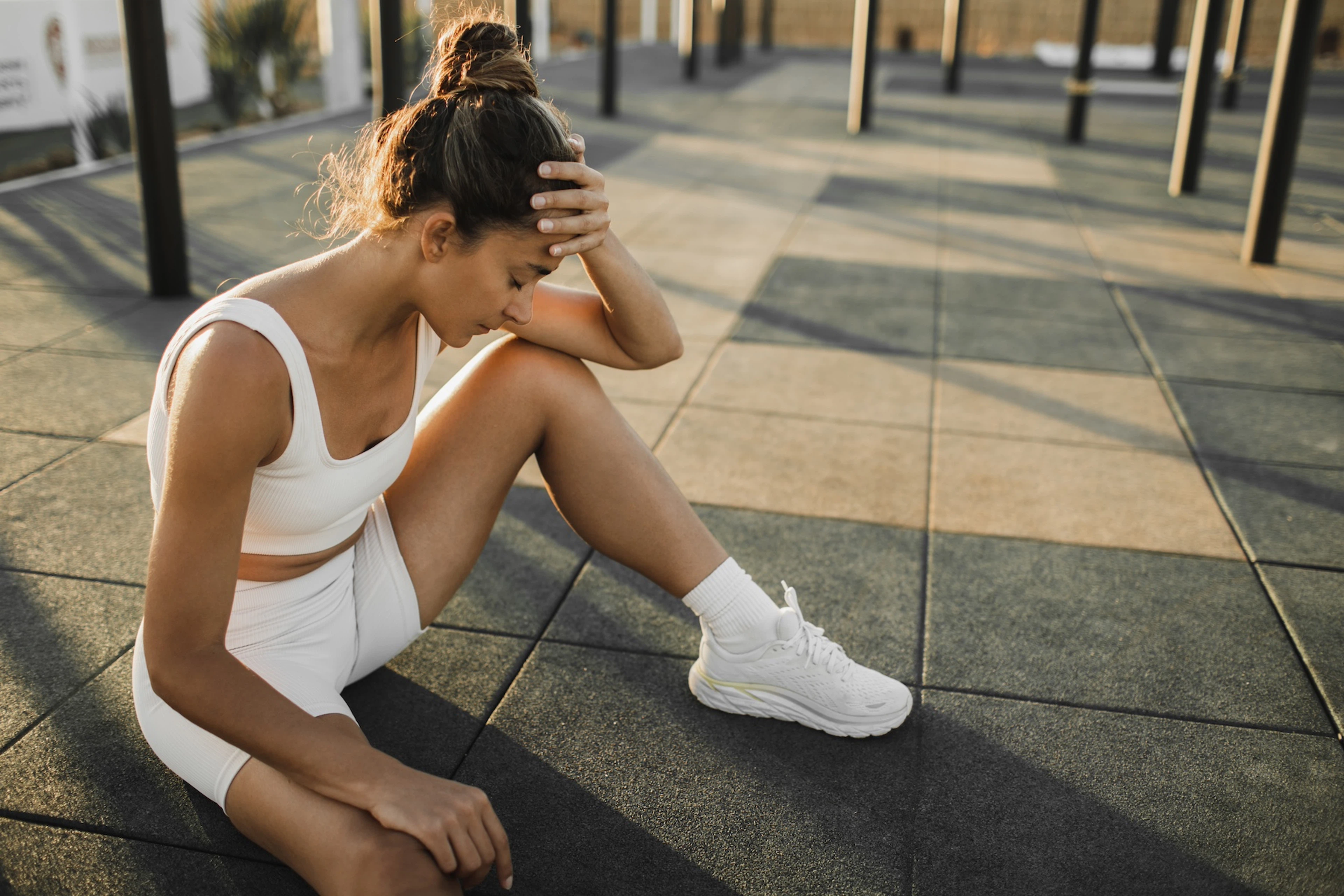 A woman sitting down and resting her head in her hand after exercise. She is experiencing signs of overtraining like fatigue.