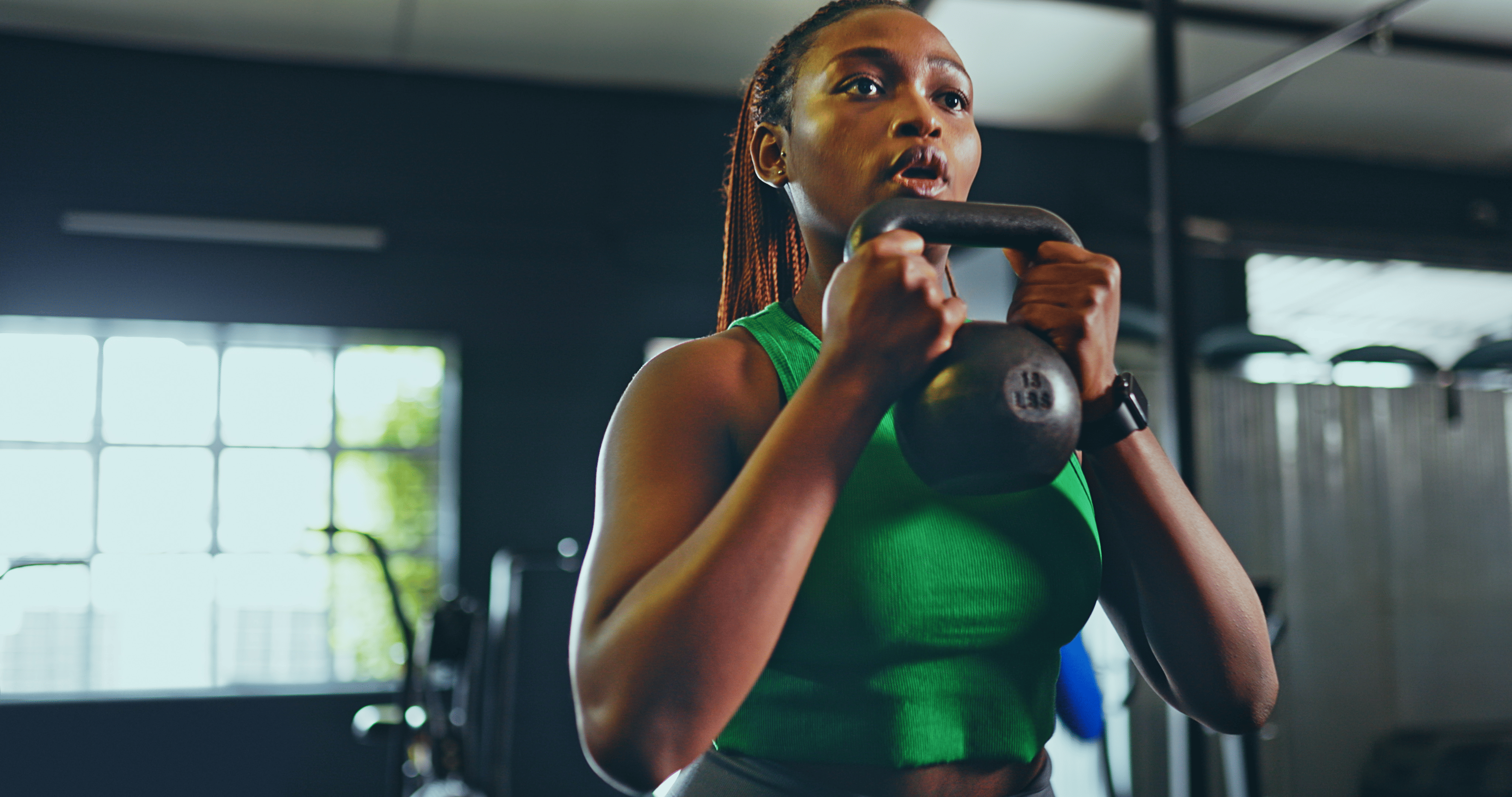 Woman holding a kettlebell in front of her chest while doing kettlebell arm exercises in a gym.