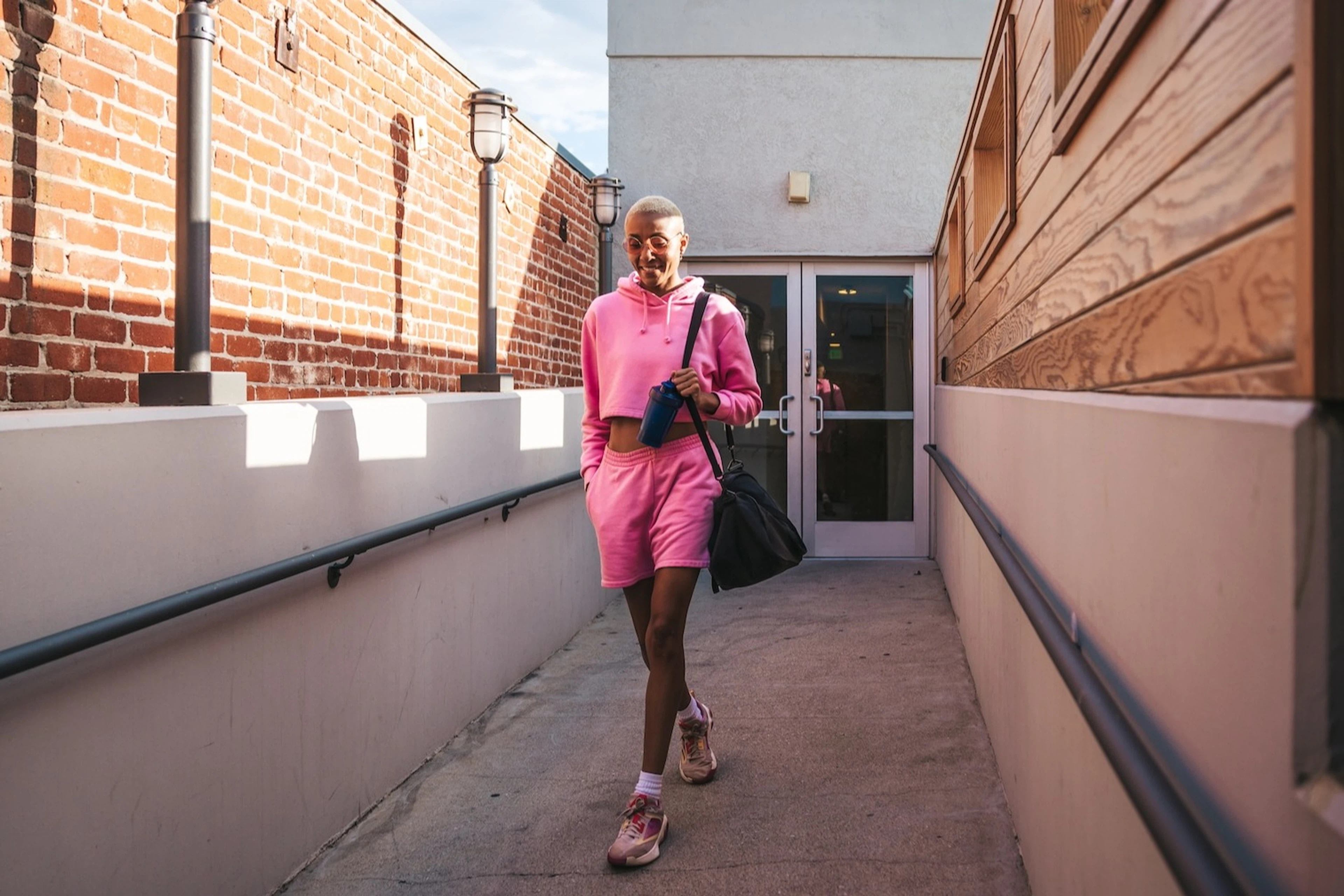 A young woman leaving the gym. She's wearing a pink outfit set with a gym bag on her shoulder. 