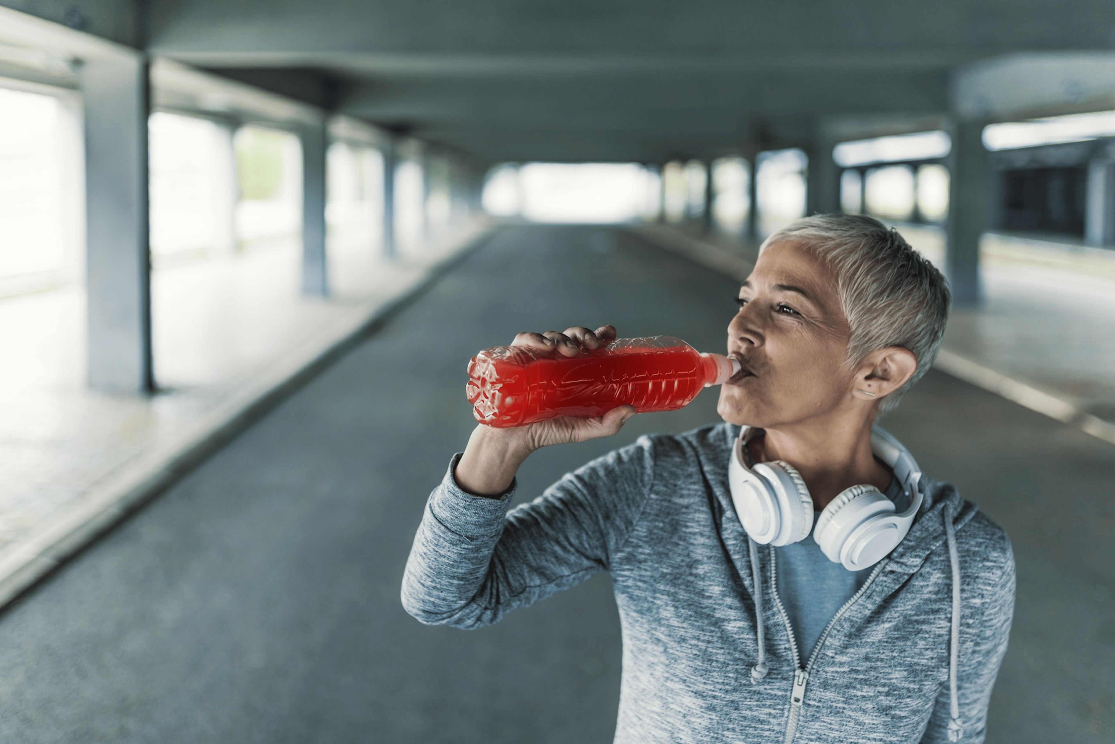 A woman drinking a sports drink from a bottle during a tough outdoor workout. 