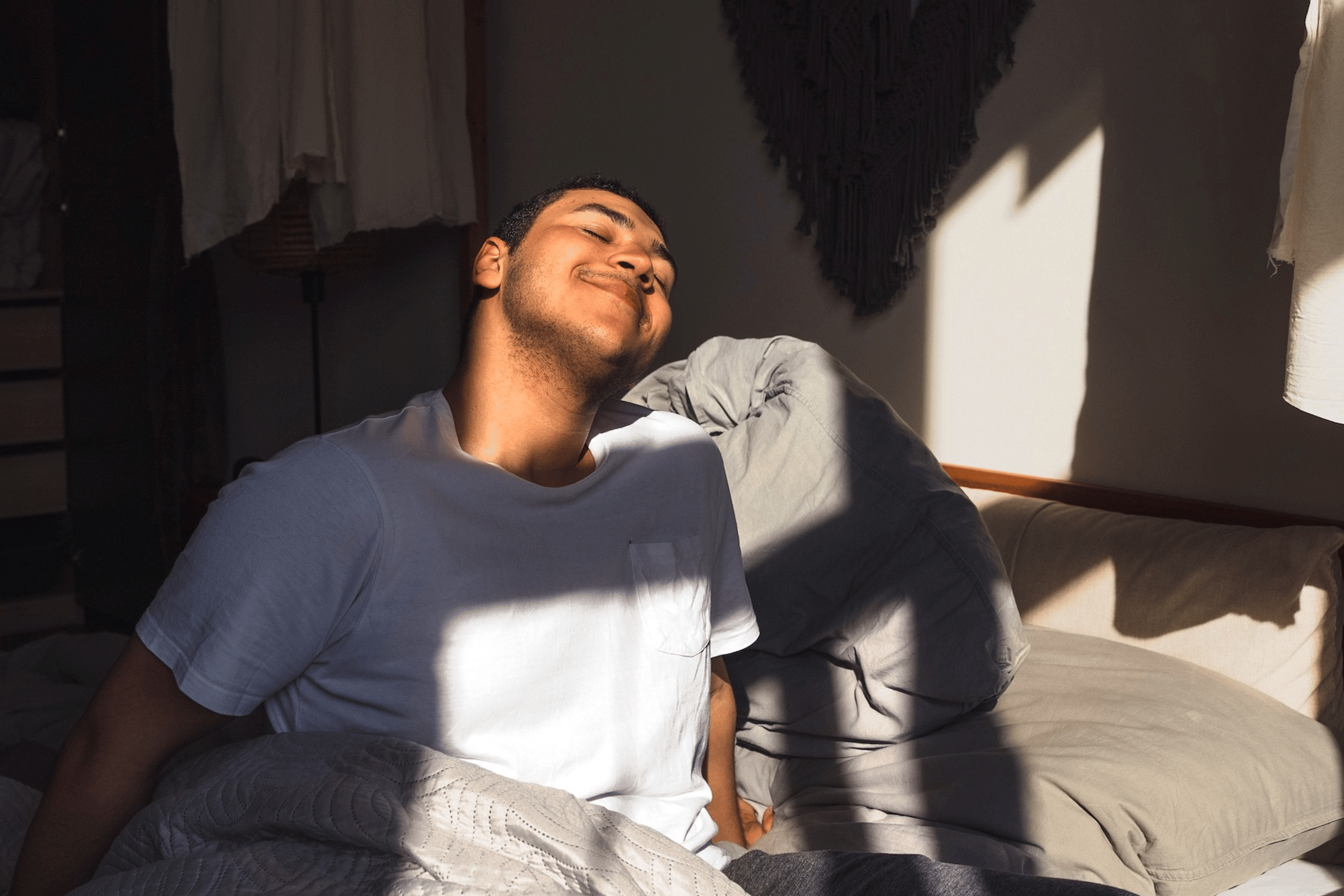 A man practicing a healthy habit of sleeping more. He is waking up happy in a sunny room after going to bed 30 minutes earlier the night before.