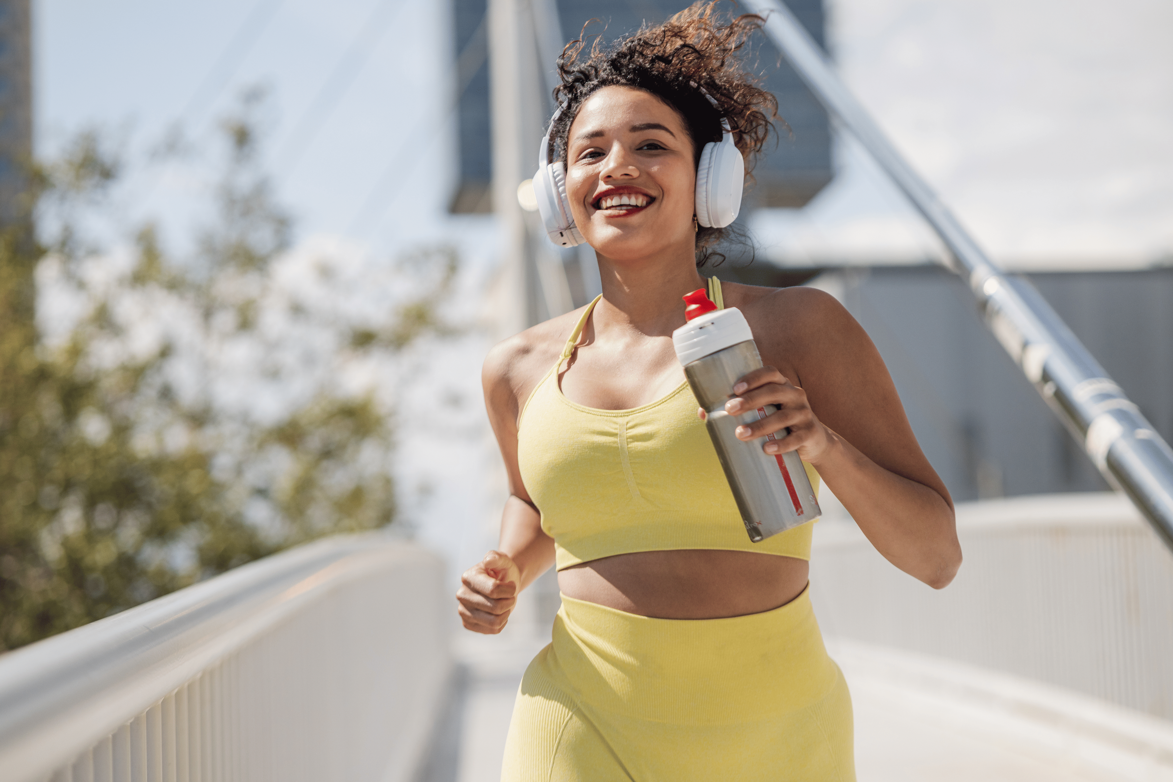 Woman running outside with headphones on holding a water bottle