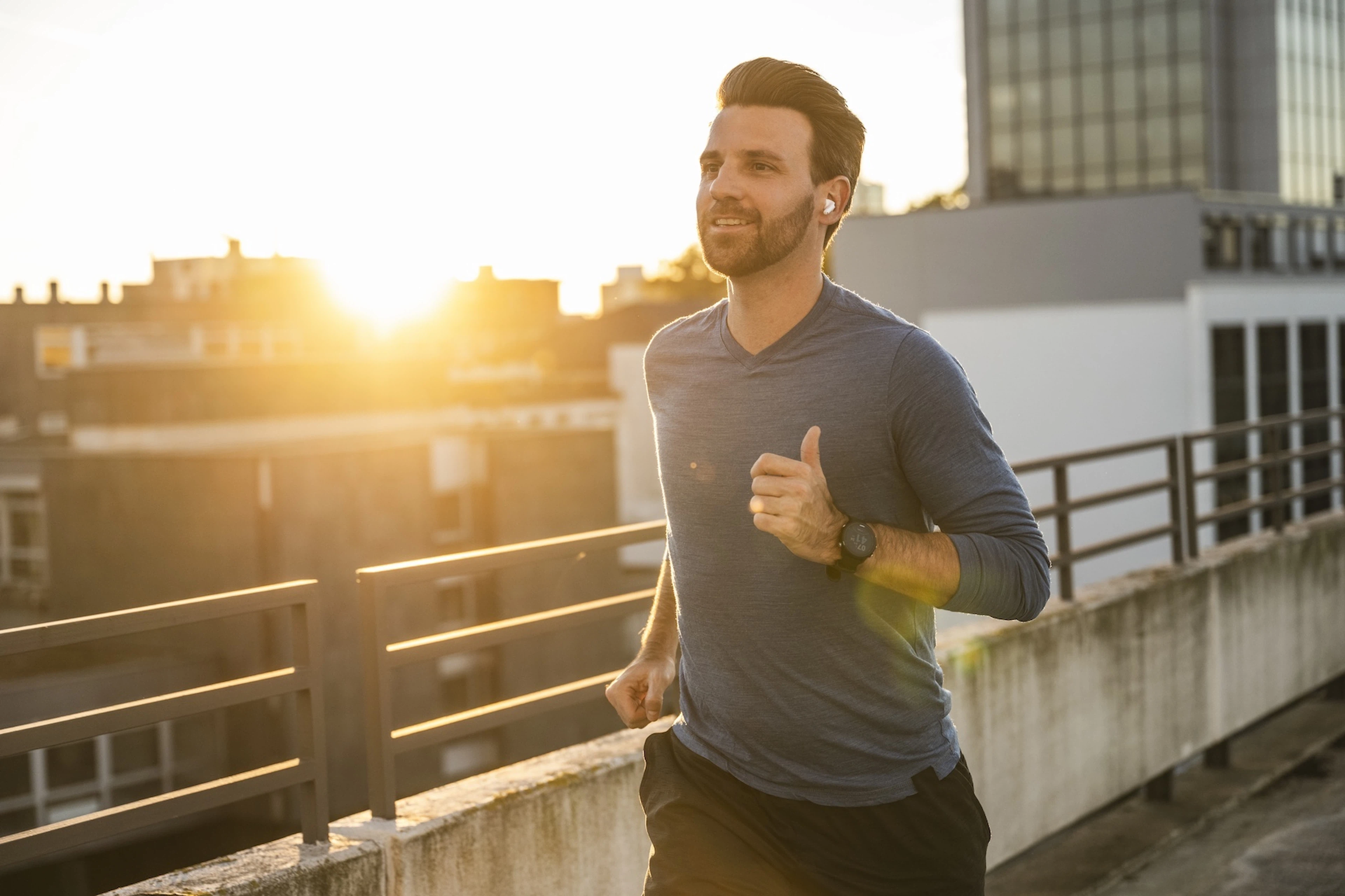 A happy man going for an outdoor jog at dusk while listening to music.