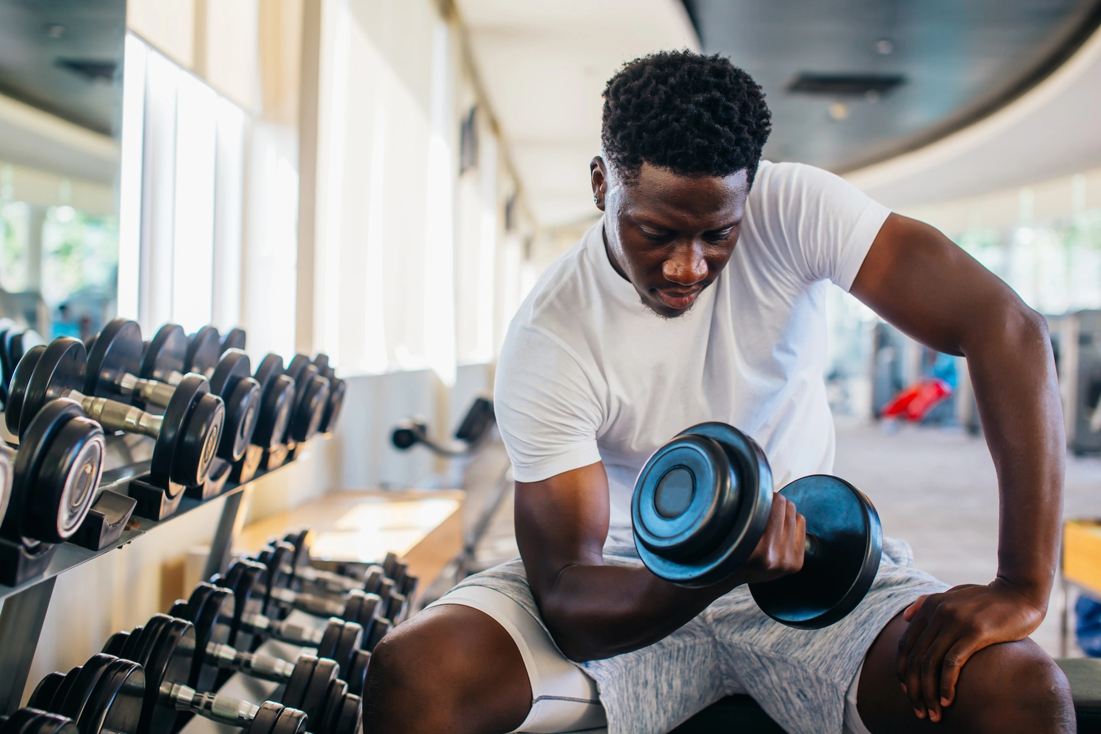 A man sitting on a workout bench and lifting a dumbbell at the gym as he trains to failure.