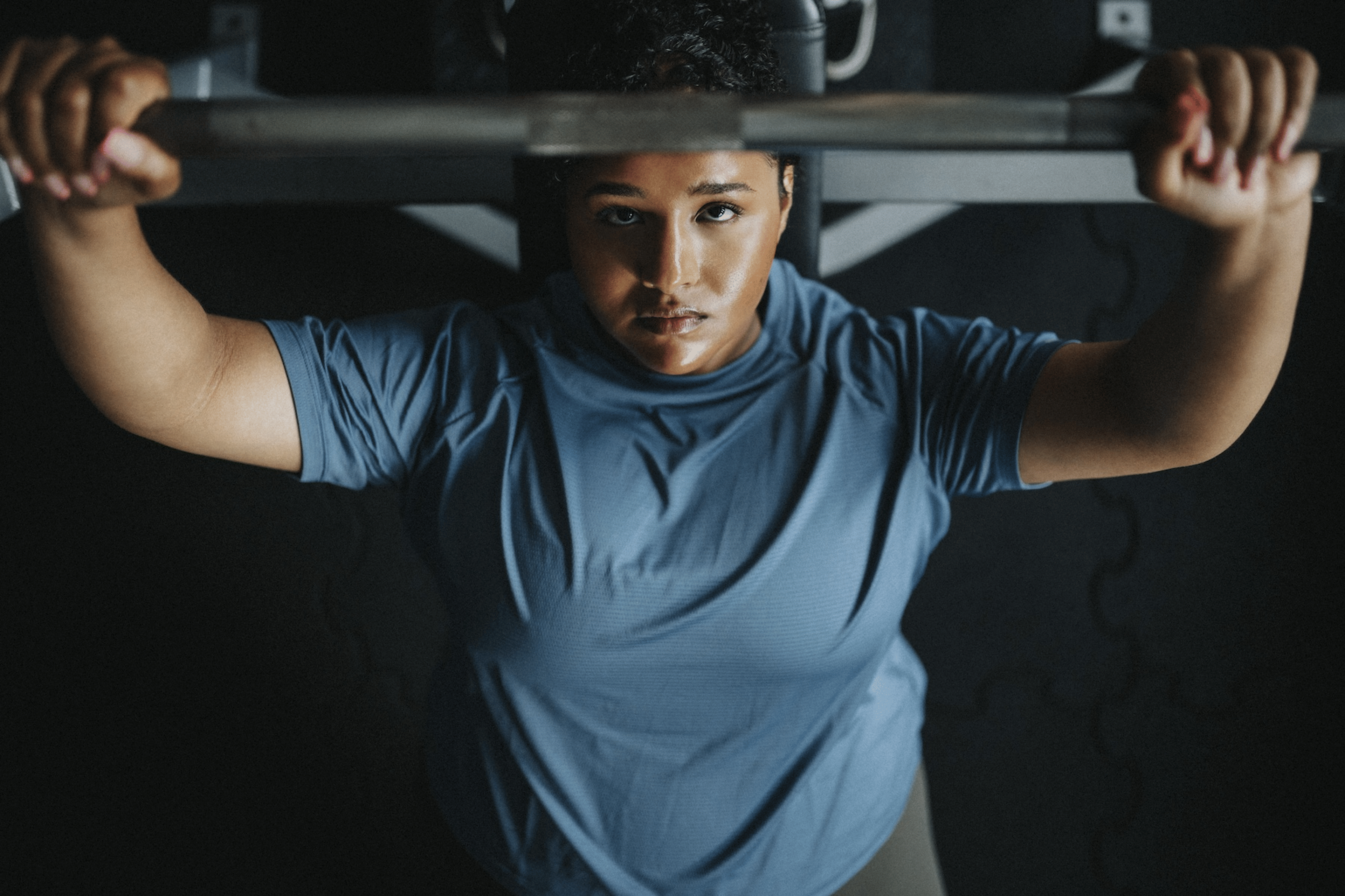 A bird's-eye view of a woman performing a bench press with a barbell at the gym.