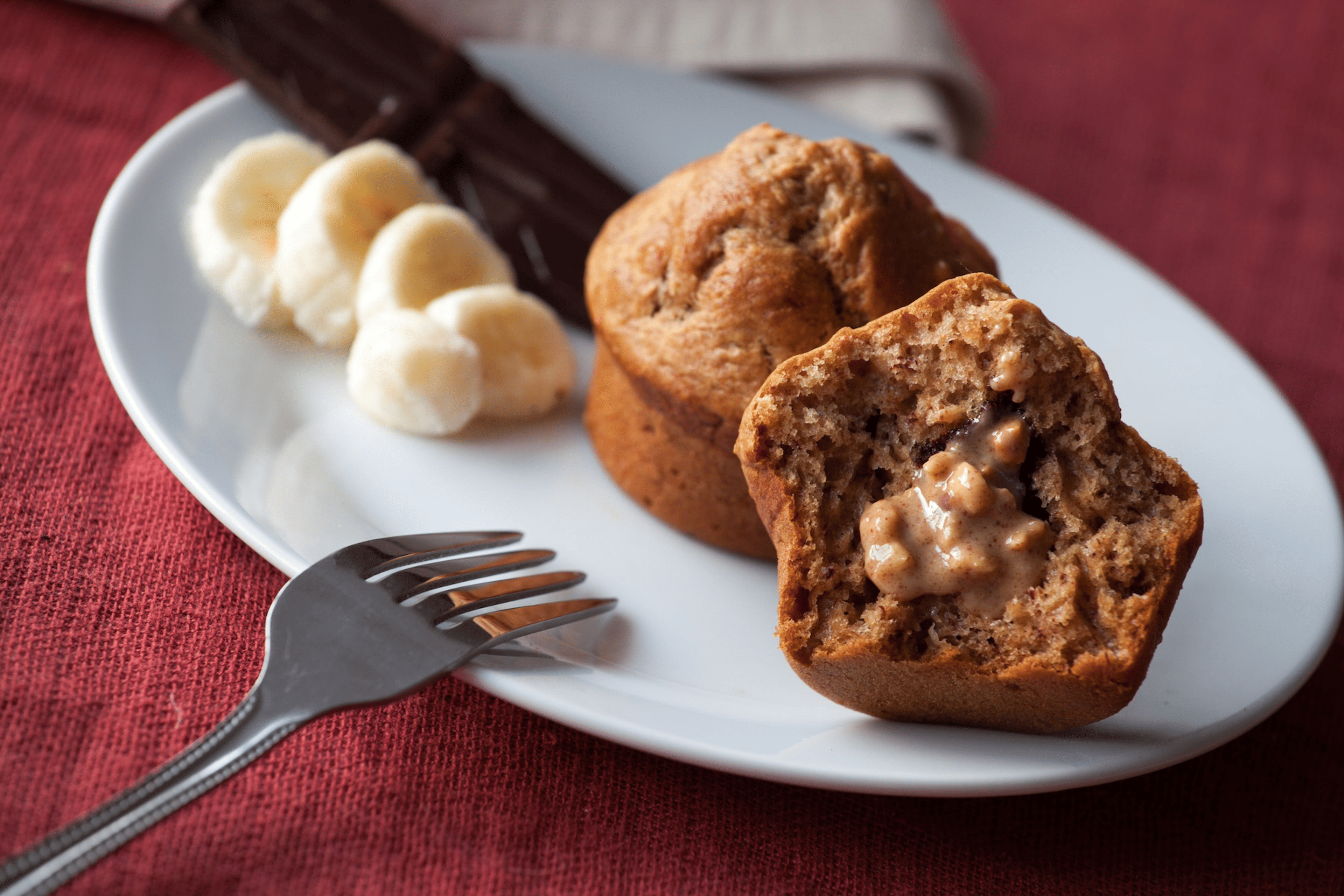 A plate with banana slices and bran muffins with peanut butter on one of the muffins, which is a high-protein snack.