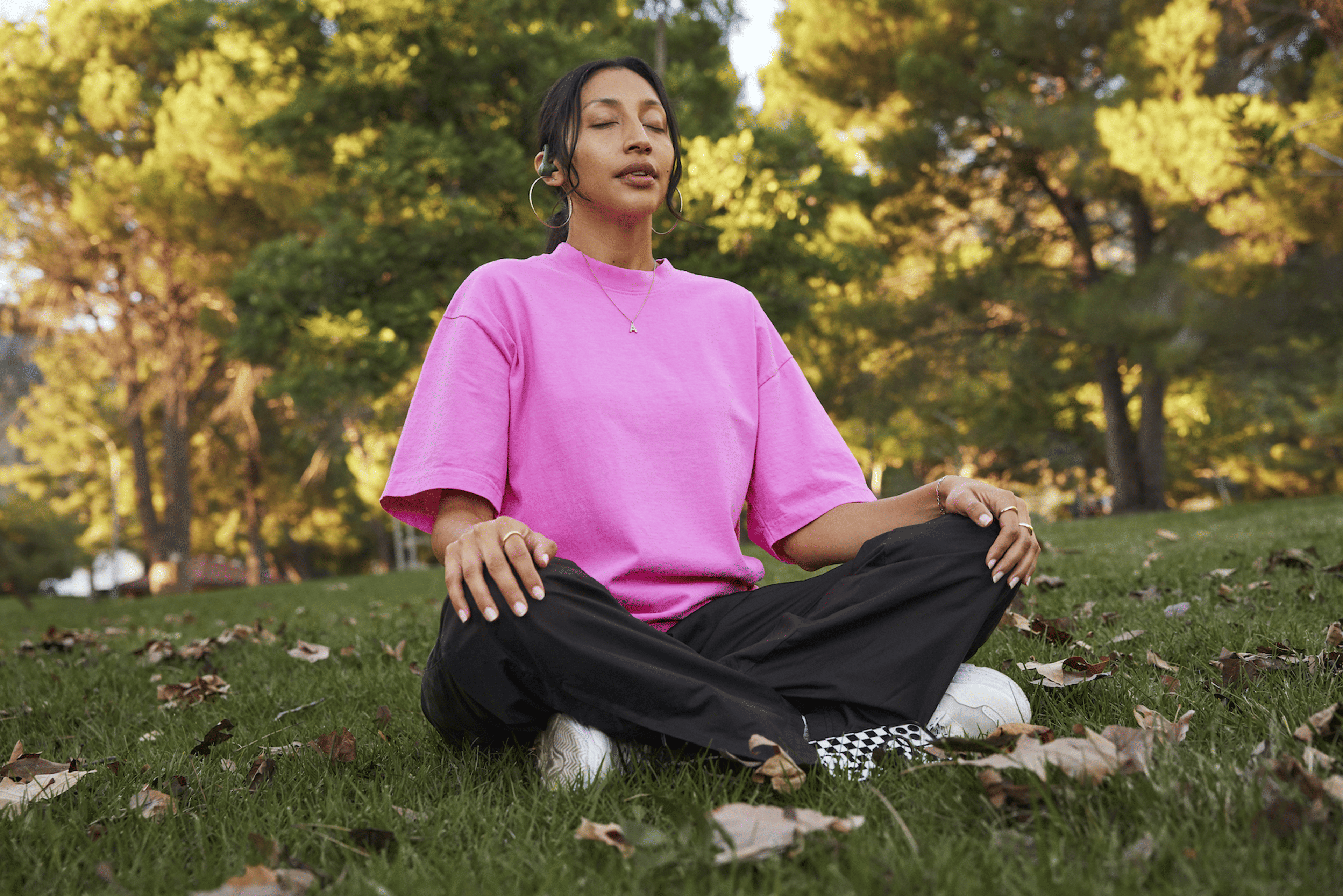 Wellness Trends: A young woman meditating while sitting in the grass.