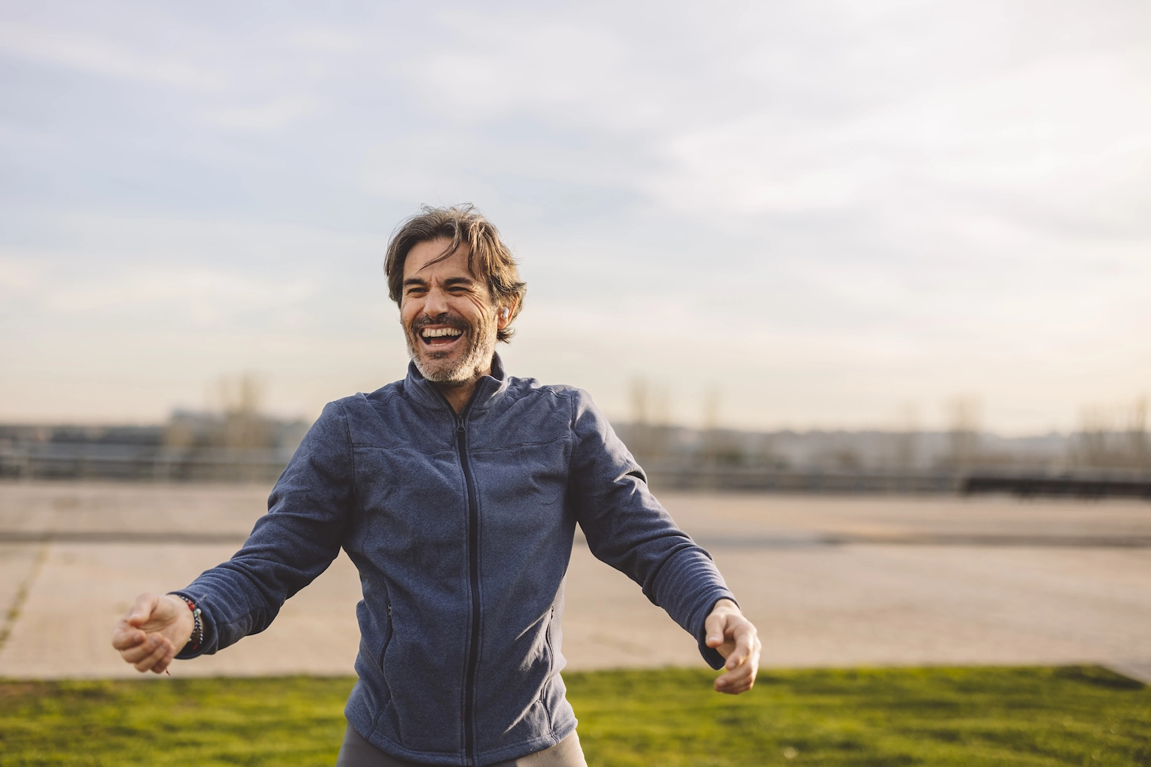 A happy man exercising outside, laughing. He views working out as a hobby.