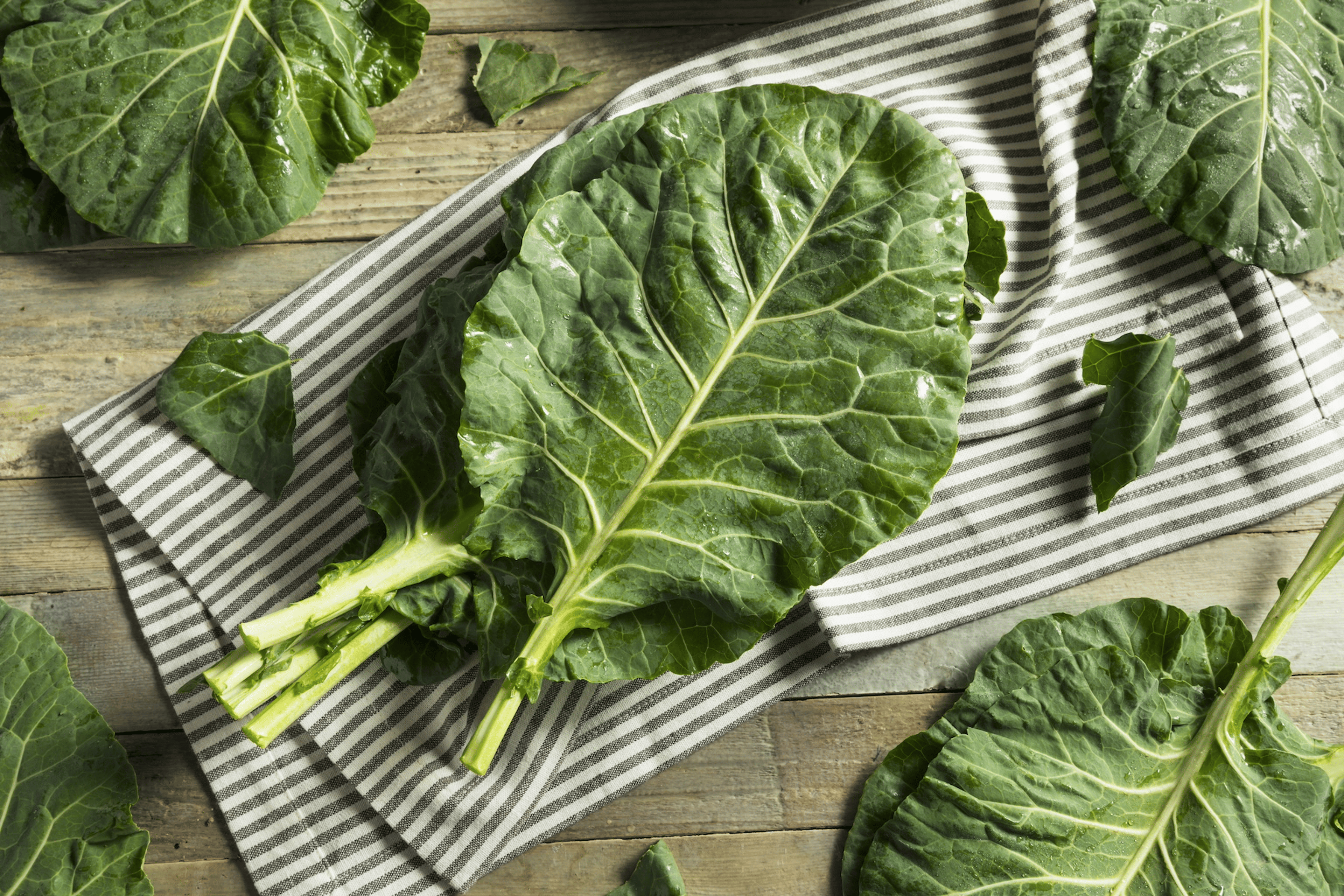 Raw collard greens resting on a towel and countertop. Collards are high-protein vegetables.