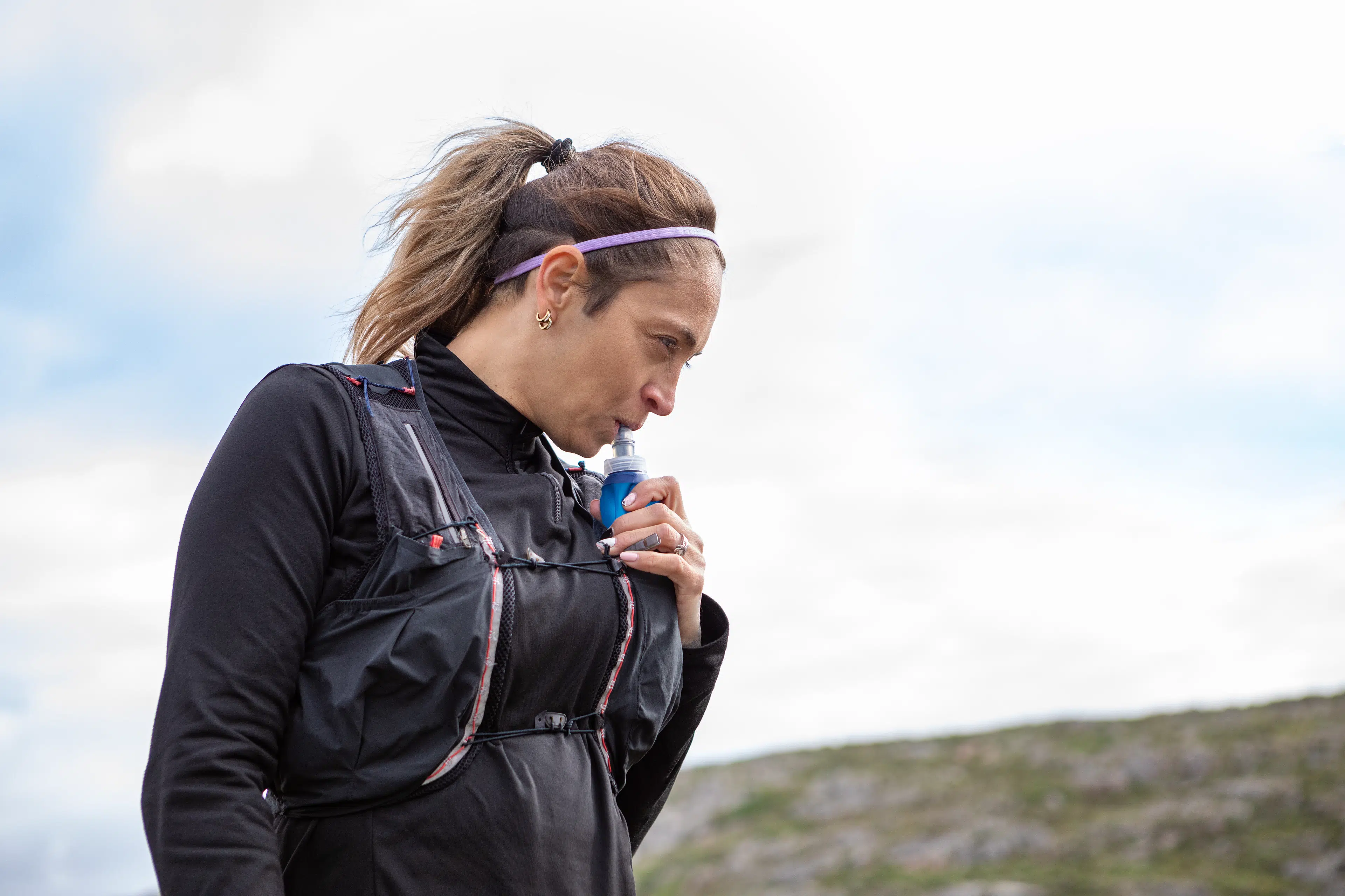 Woman drinking water out of a hydration vest while on a Peloton marathon training plan run.