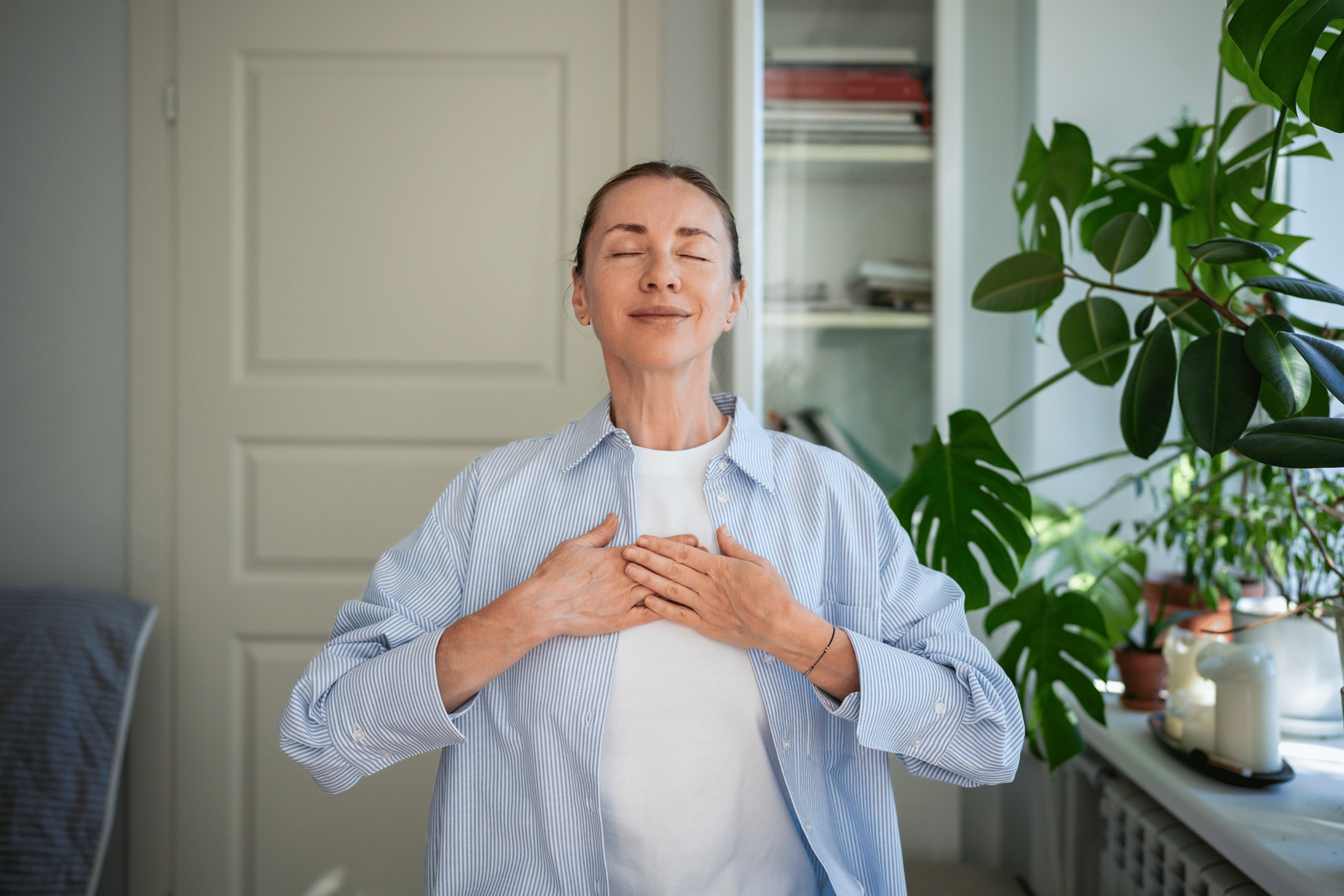 A woman meditating at home with her hands on her chest.