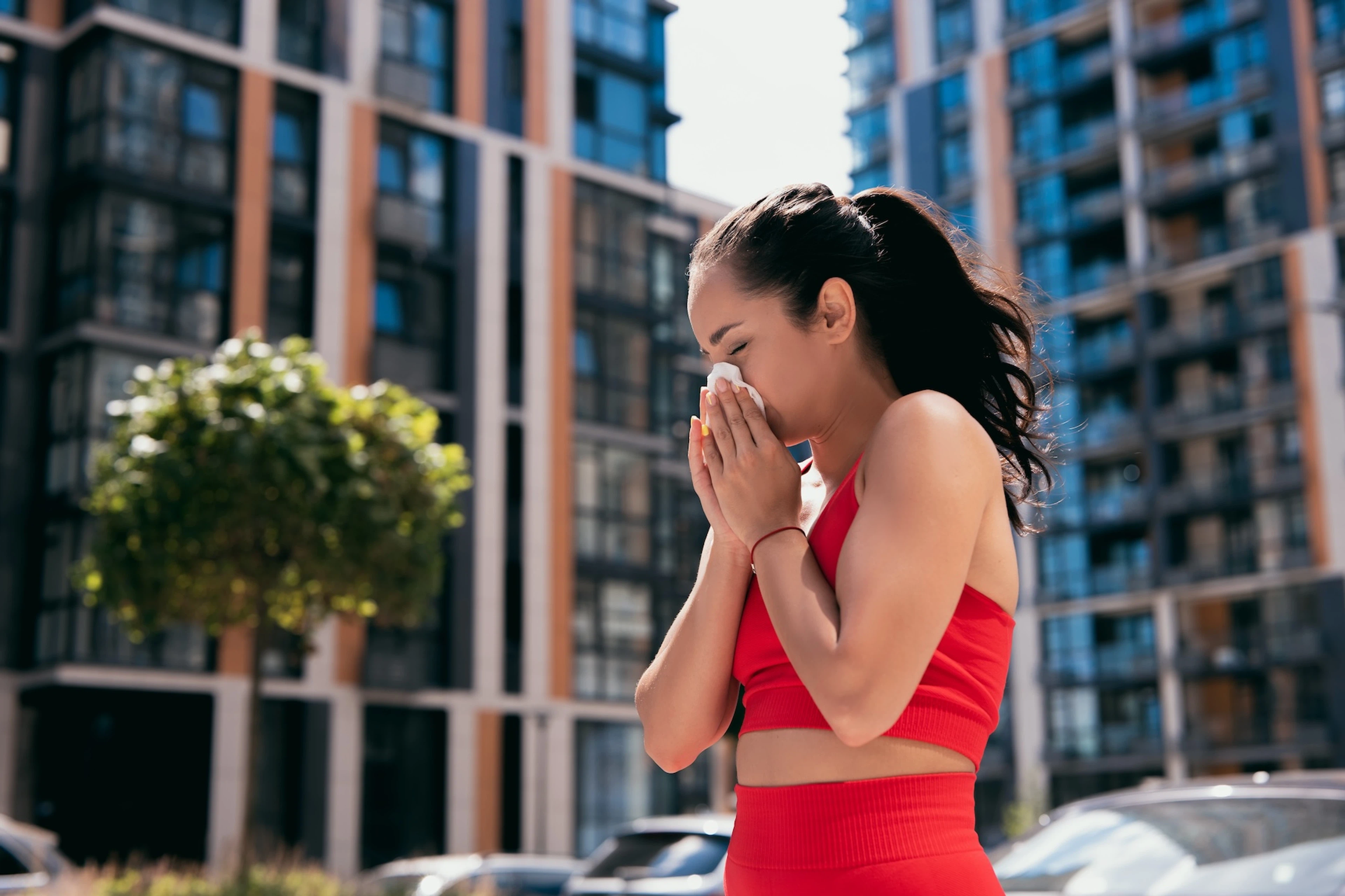 An athlete blowing her nose with a tissue outdoors because her nose is runs when she exercises.