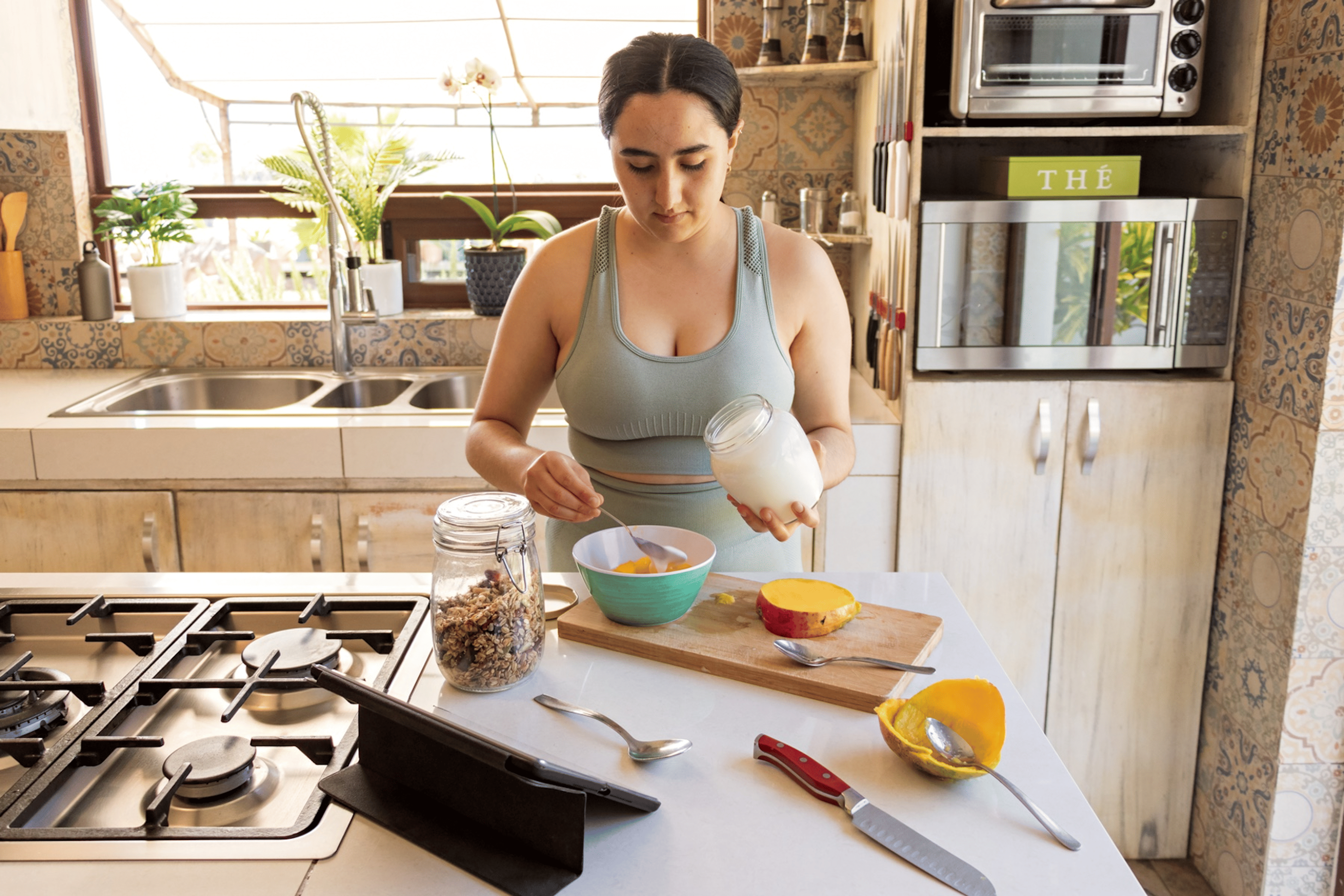 A woman preparing a bowl of yogurt with granola in her kitchen after a workout. 