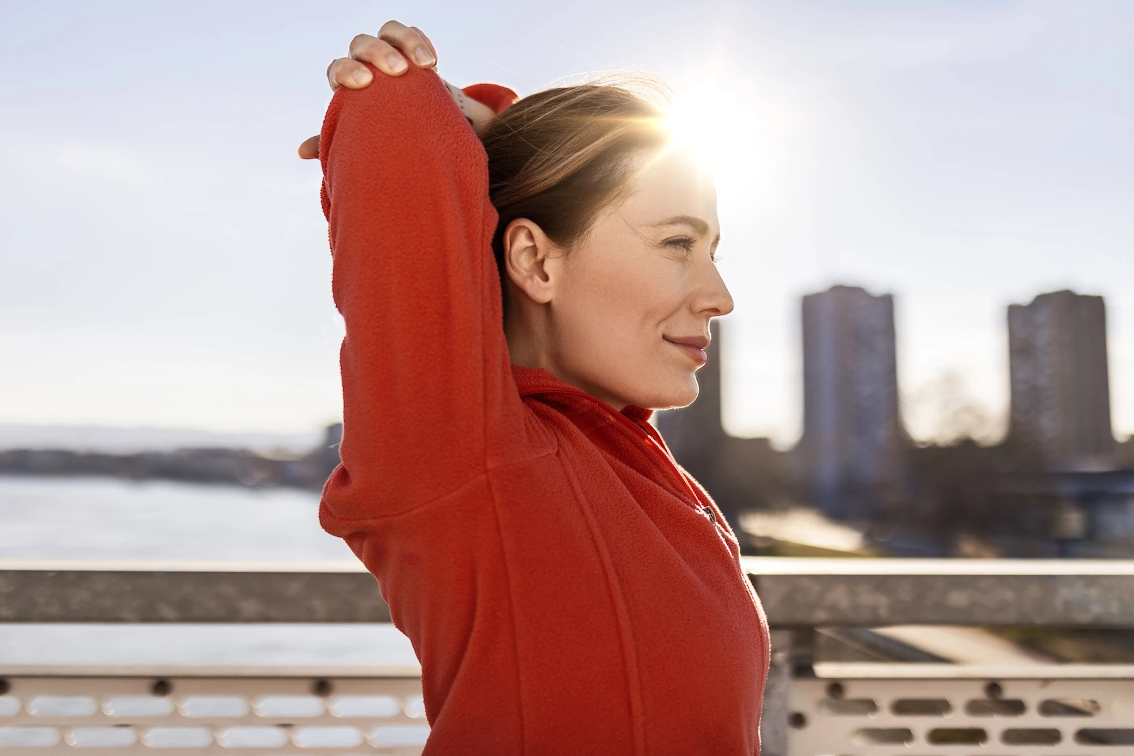 A woman happily breathing with her arms resting above her head after she finishes a morning outdoor workout.