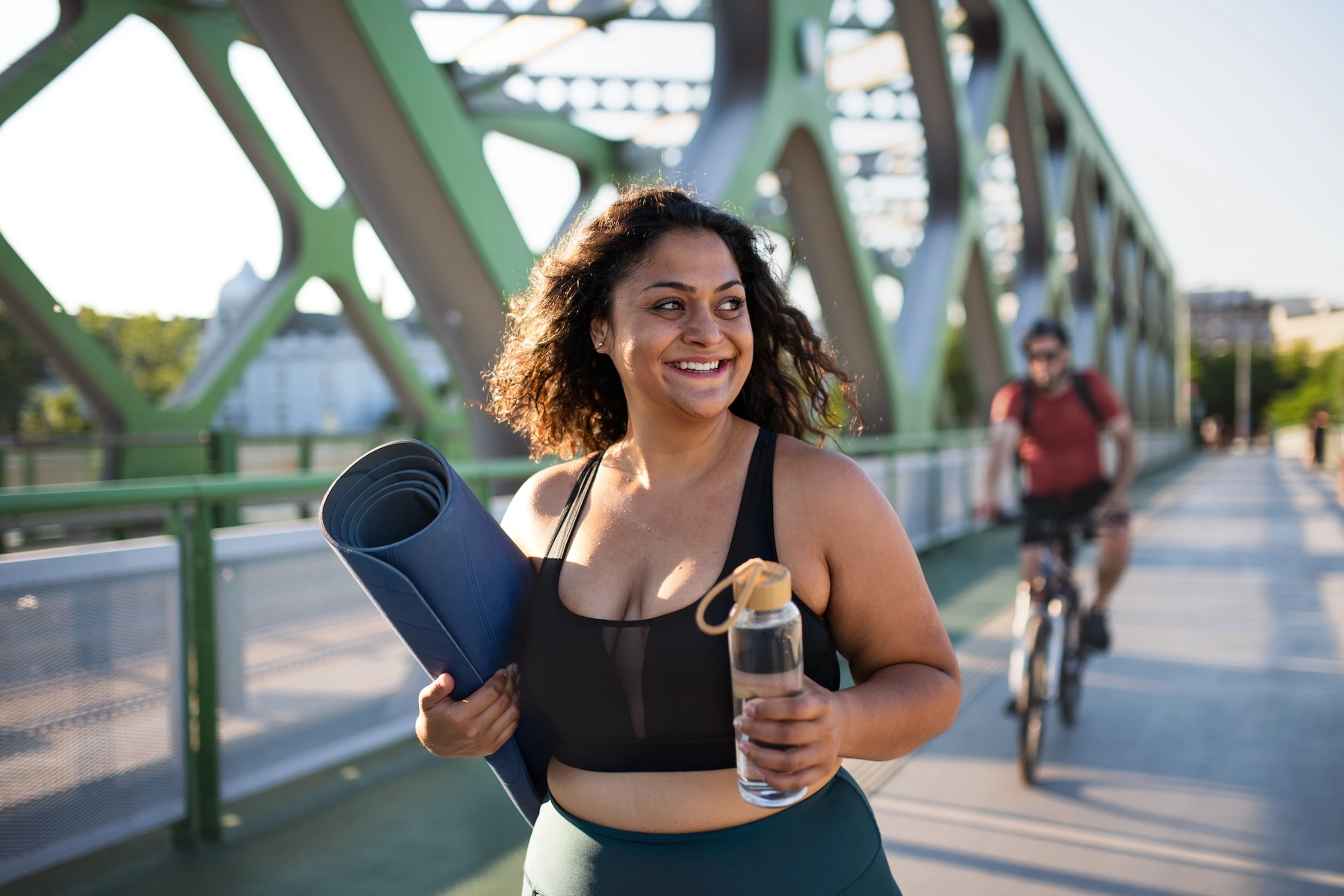 A woman going for a walk after her yoga workout. She's smiling and walking on a bridge.