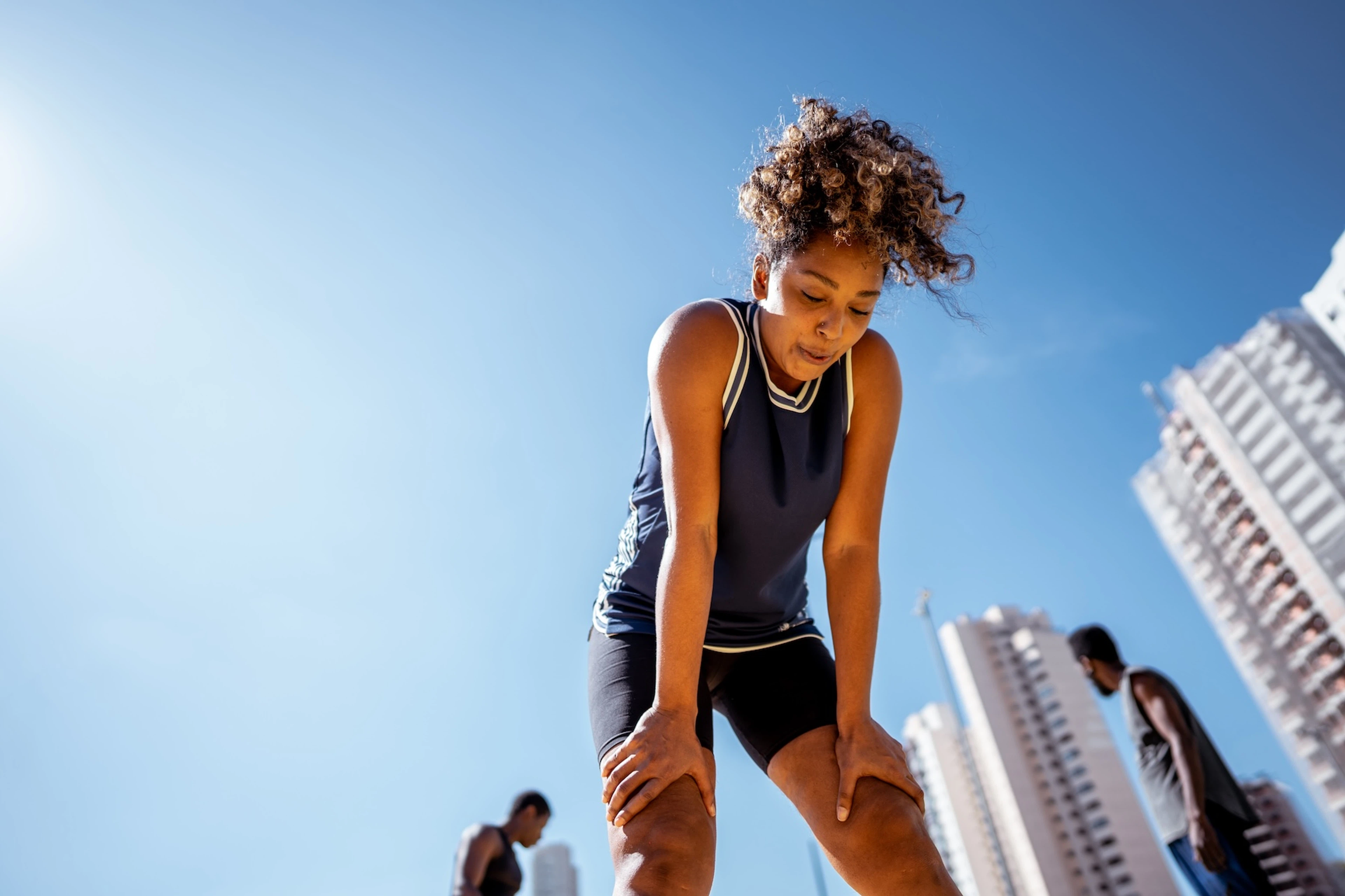 An athlete breathing deeply to calm her nerves. Her hands on her knees and she is outside.