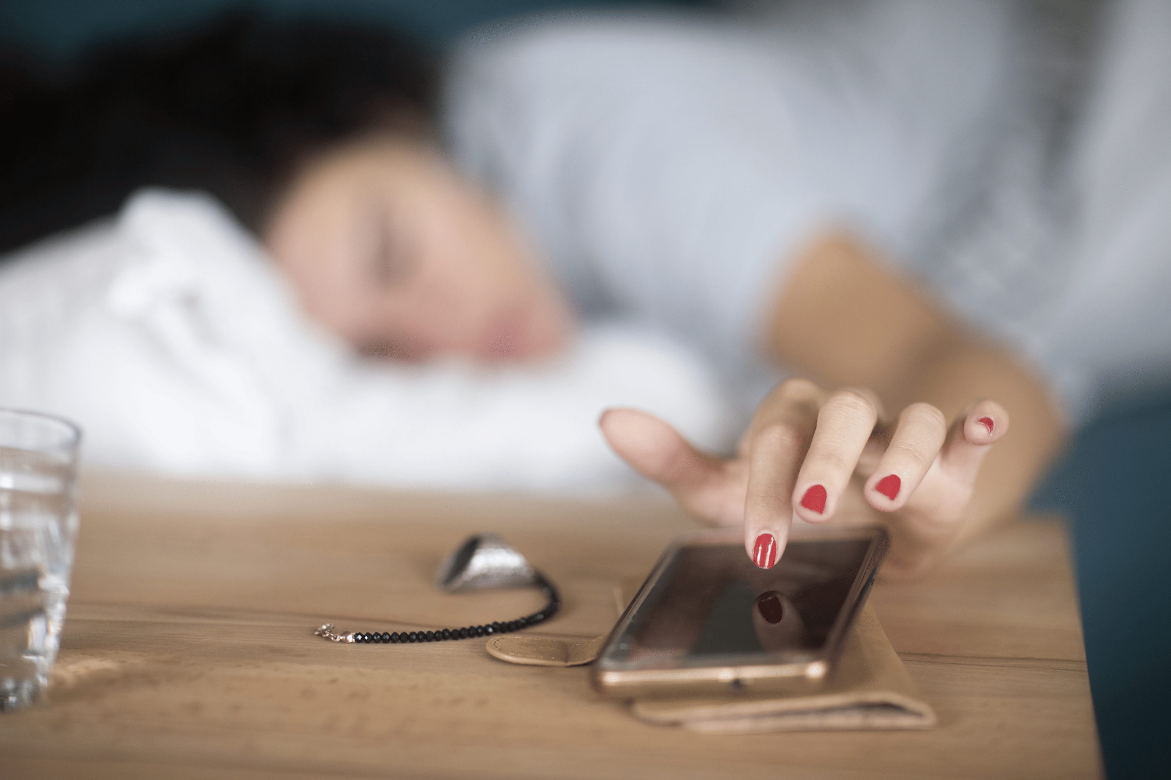 A woman snoozing her alarm on her phone as she lies in bed.
