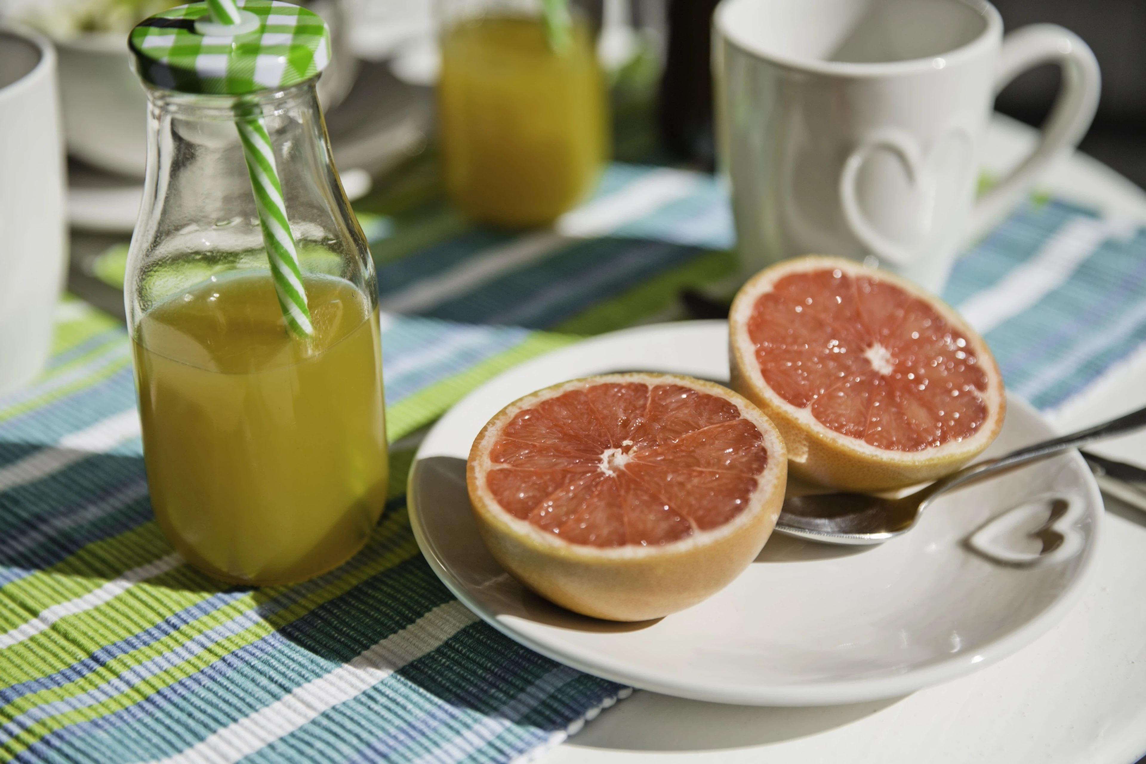 A plate with a grapefruit cut in half next to a bottle of fresh orange juice, both of which are hydrating foods and drinks.