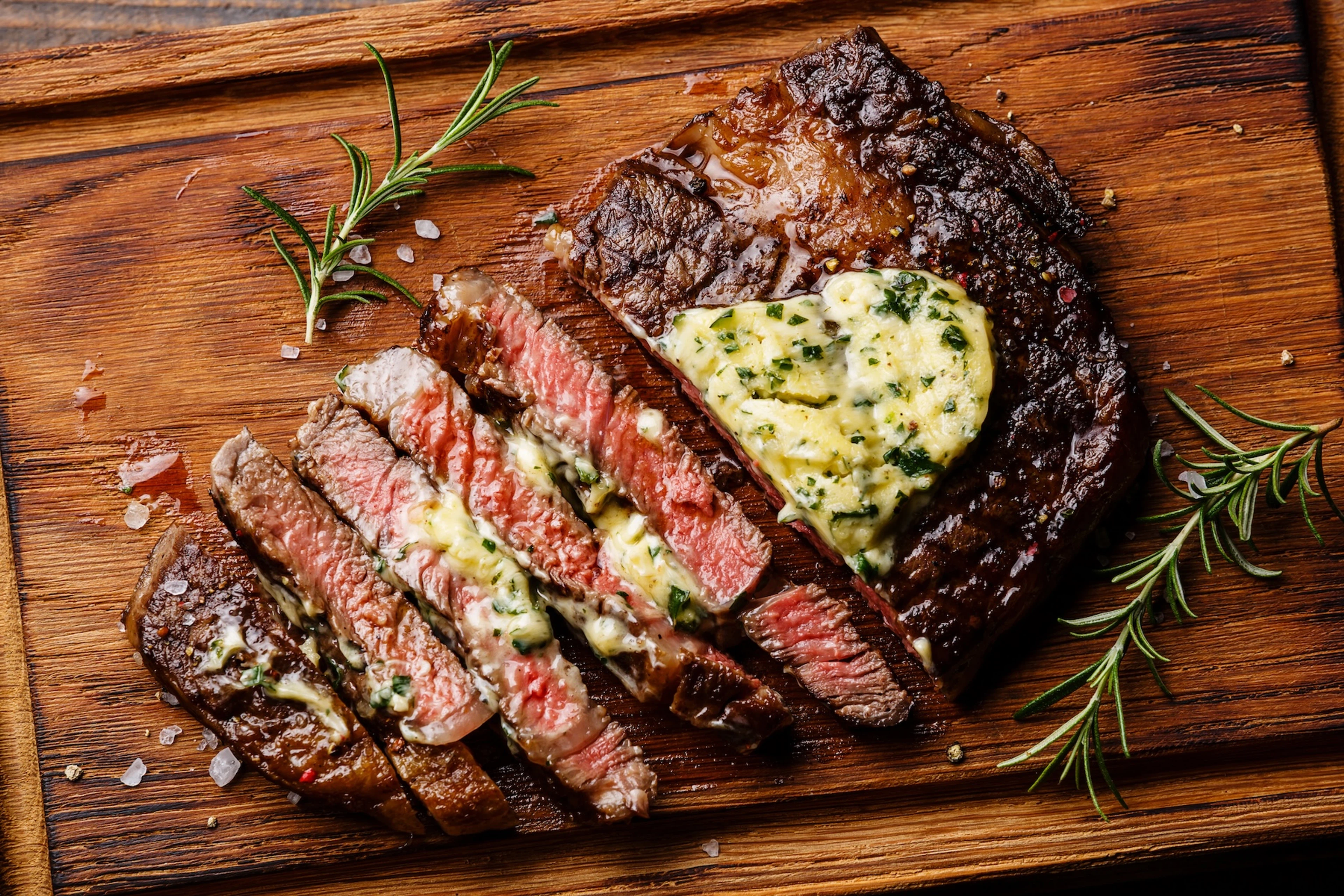 A wooden cutting board with a steak (which is a creatine-rich food) sliced up and garnished with herb butter.