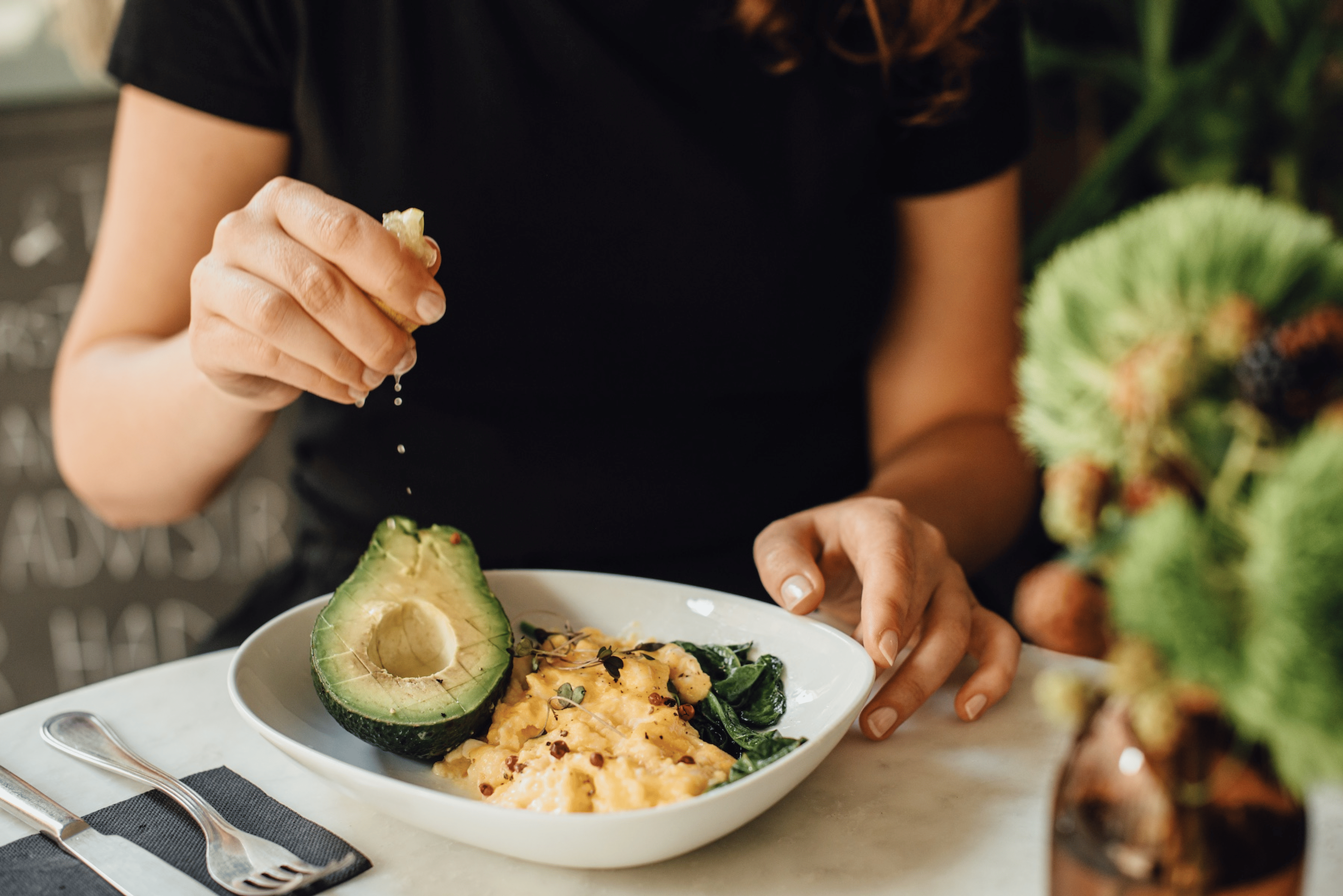 A woman eating scrambled eggs and half an avocado for a meal. She's squeezing a lemon slice on the avocado.