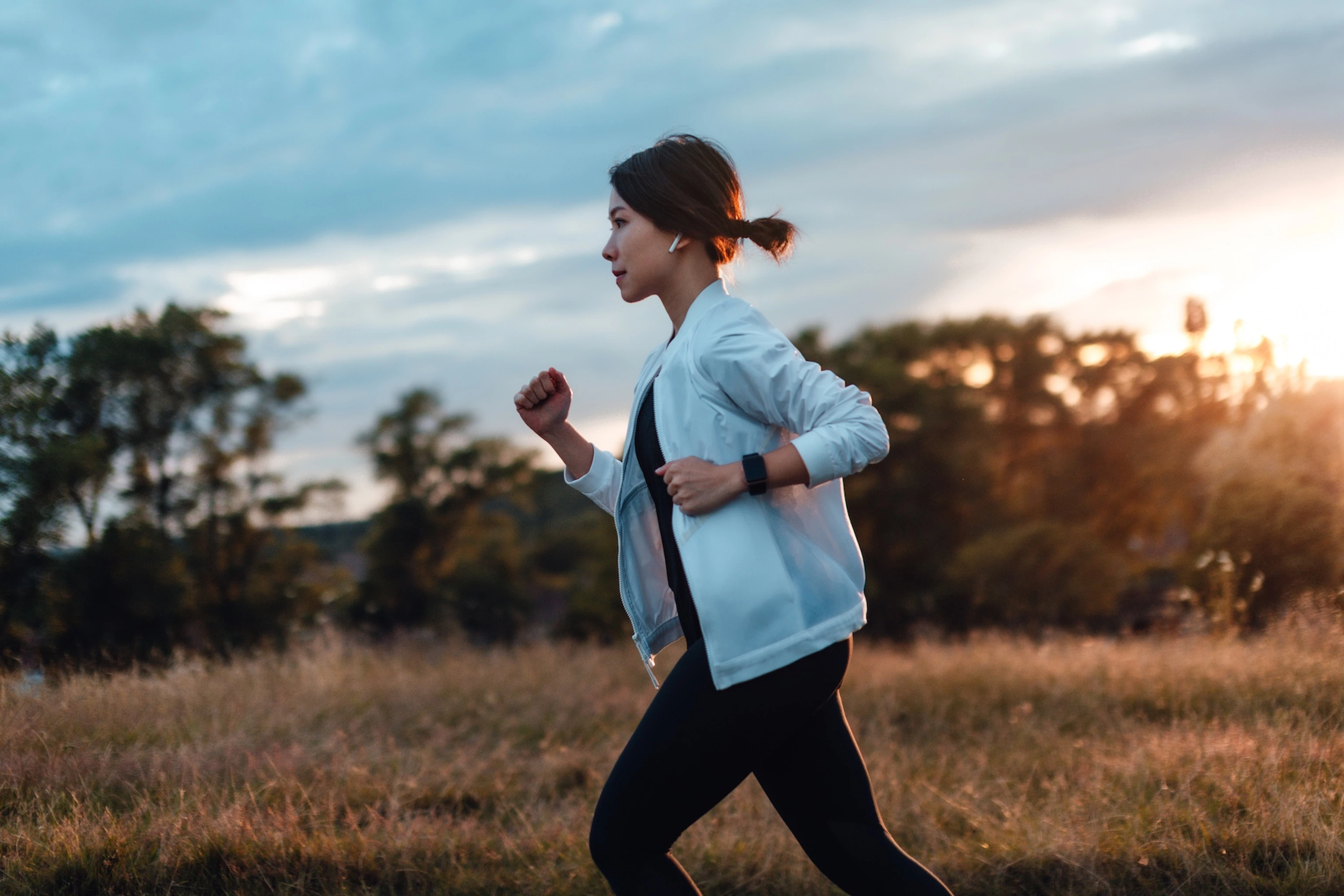 A woman working to improve her cardiovascular endurance by going on a jog in the park at dusk.