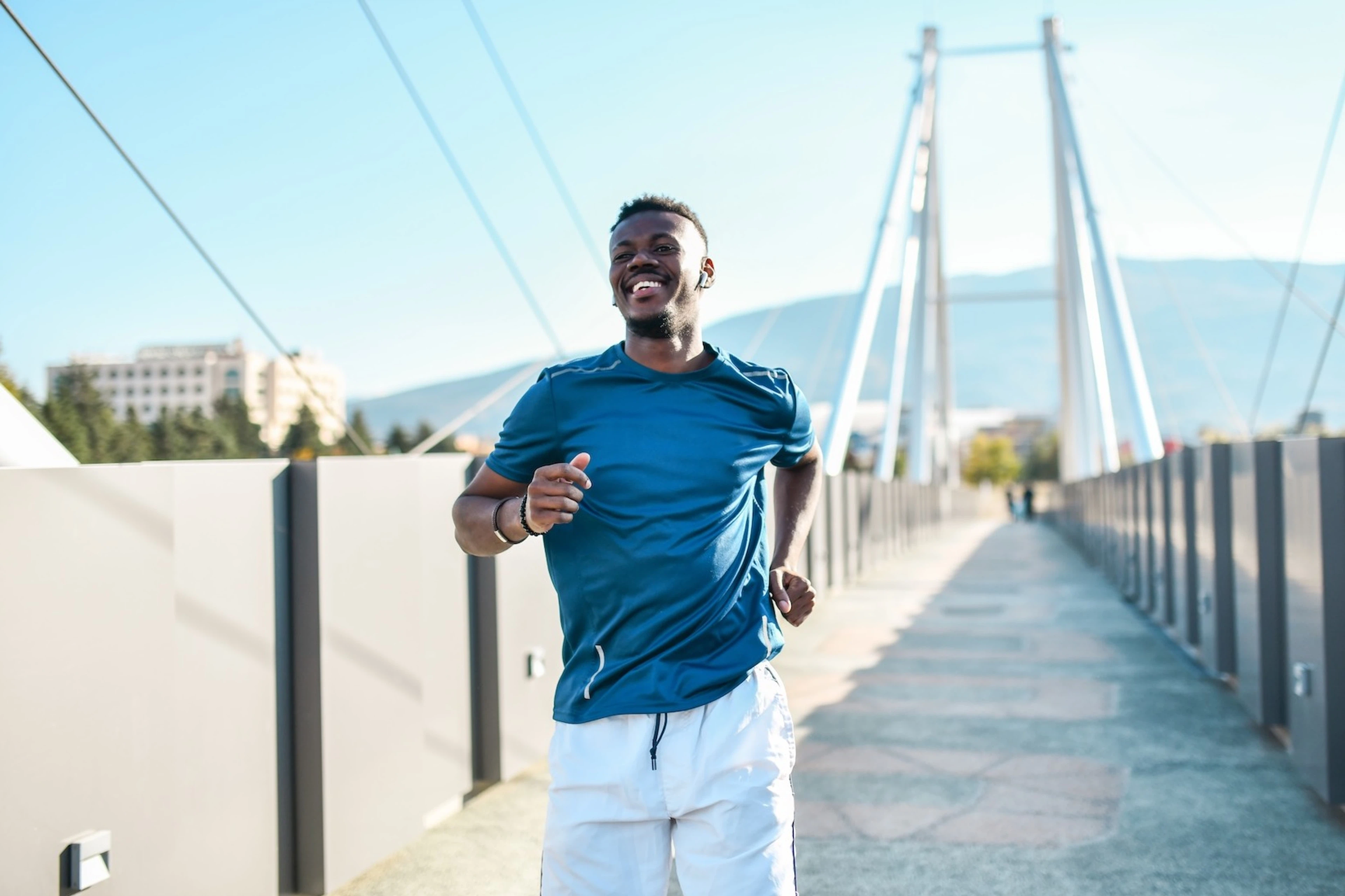 A smiling man running across a bridge on a sunny day.
