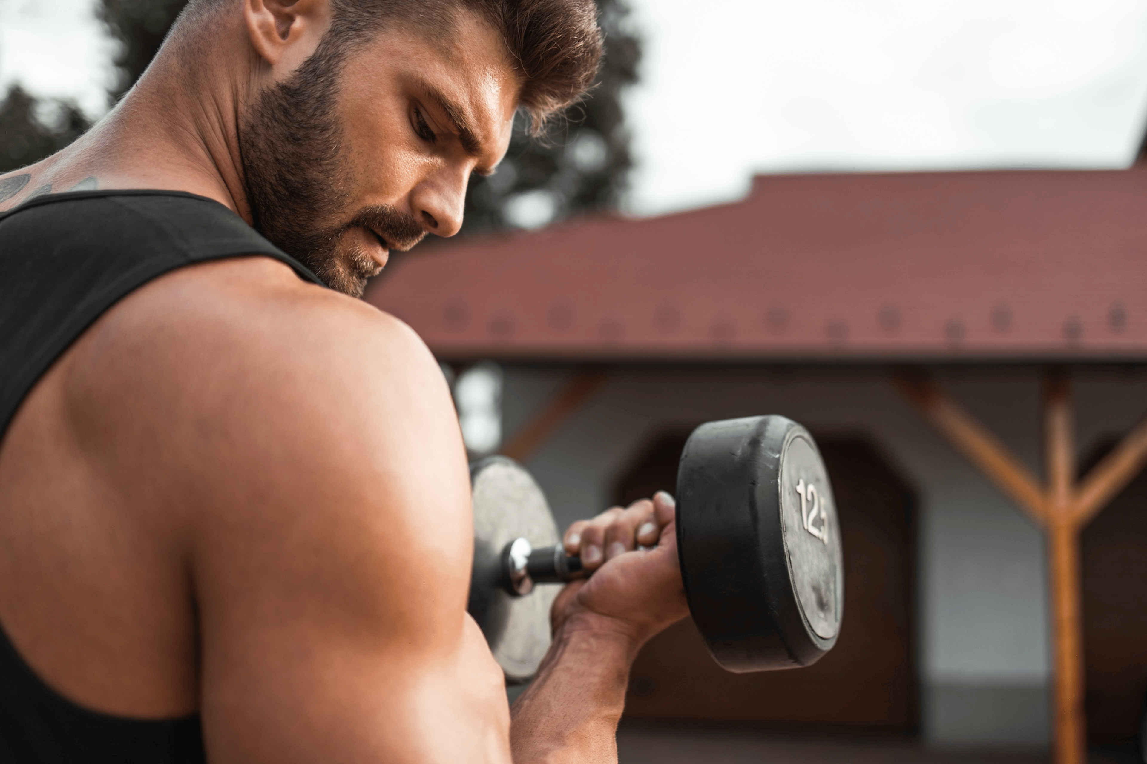 A man performing a bicep curl with a dumbbell outside while training to failure.