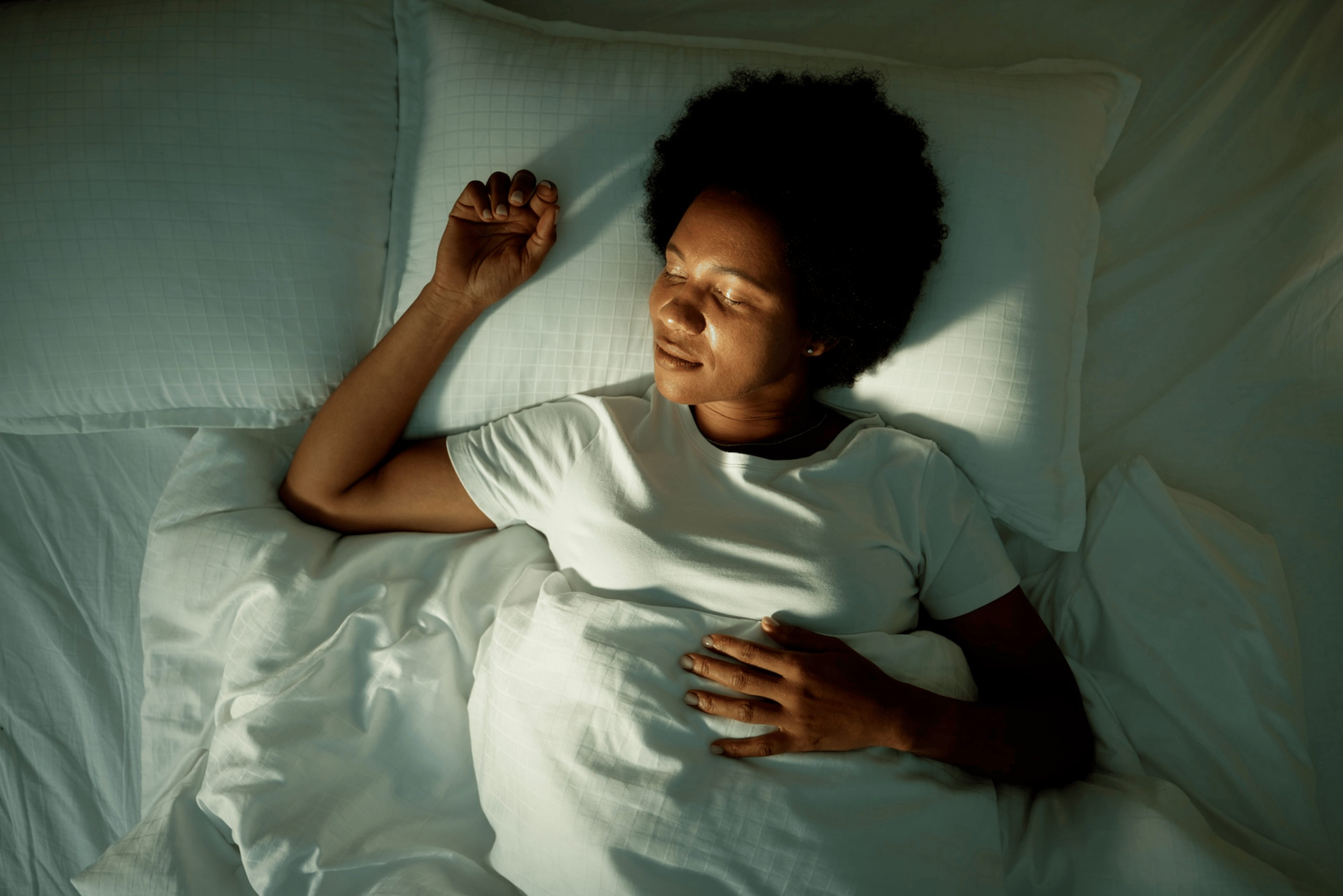 A woman practicing sleep meditation in bed. She's lying on her back under the covers with her eyes closed.