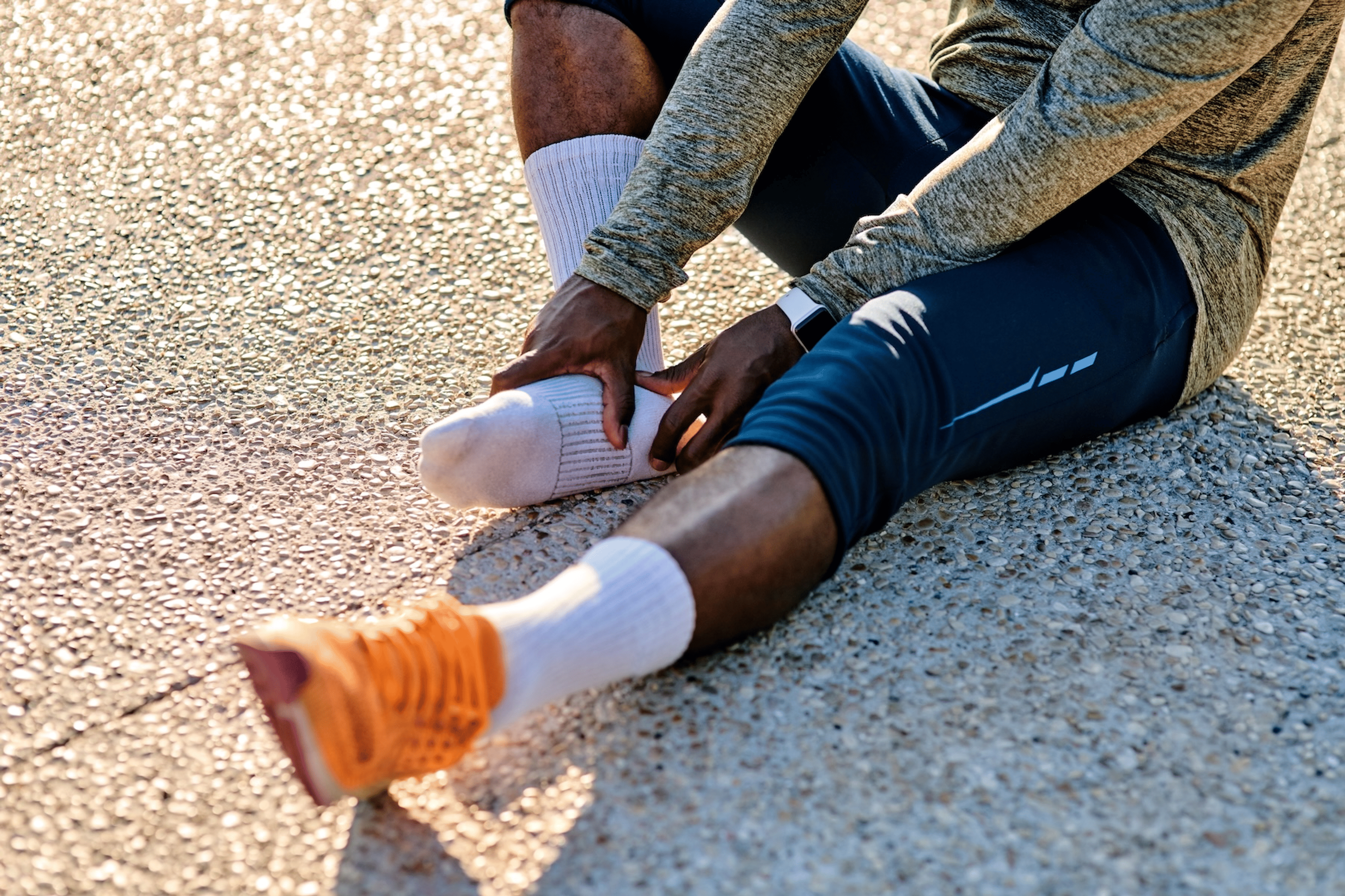 A close-up photo of a runner sitting on the ground, rubbing one of their feet as they deal with numb feet when running.