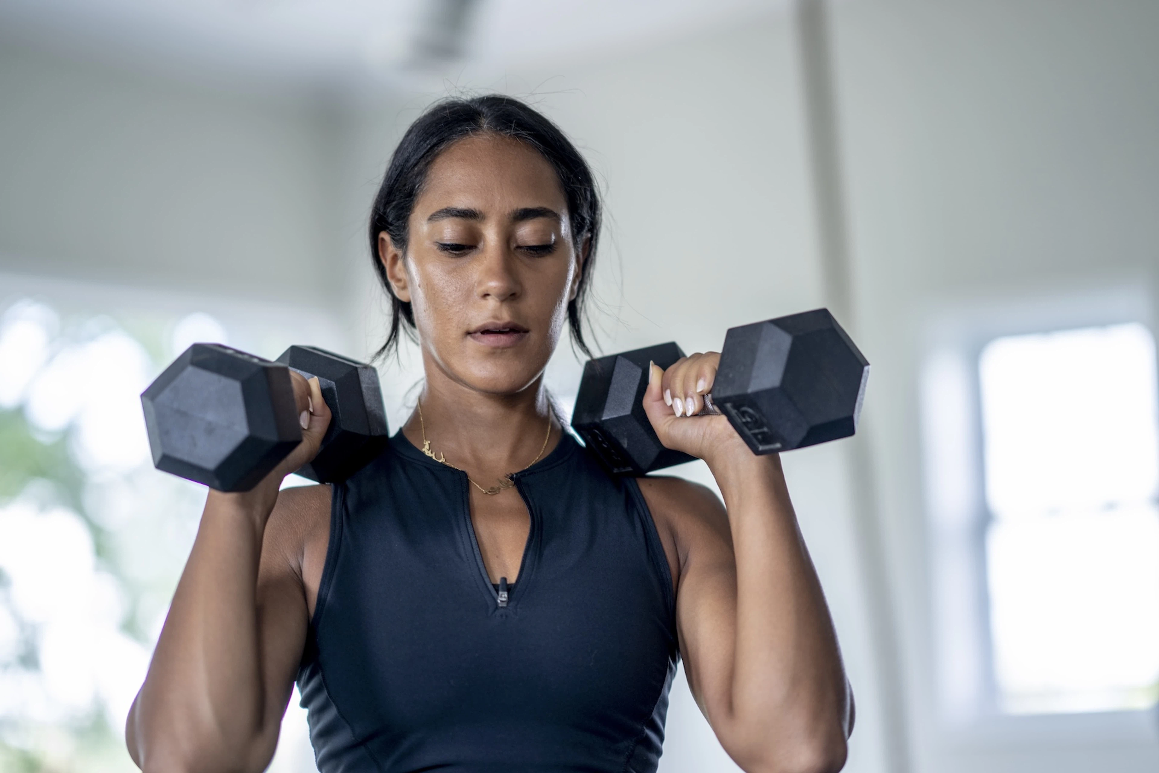 A woman working out efficiently. She is preparing to do a compound exercise with her dumbbells and an overhead press movement.