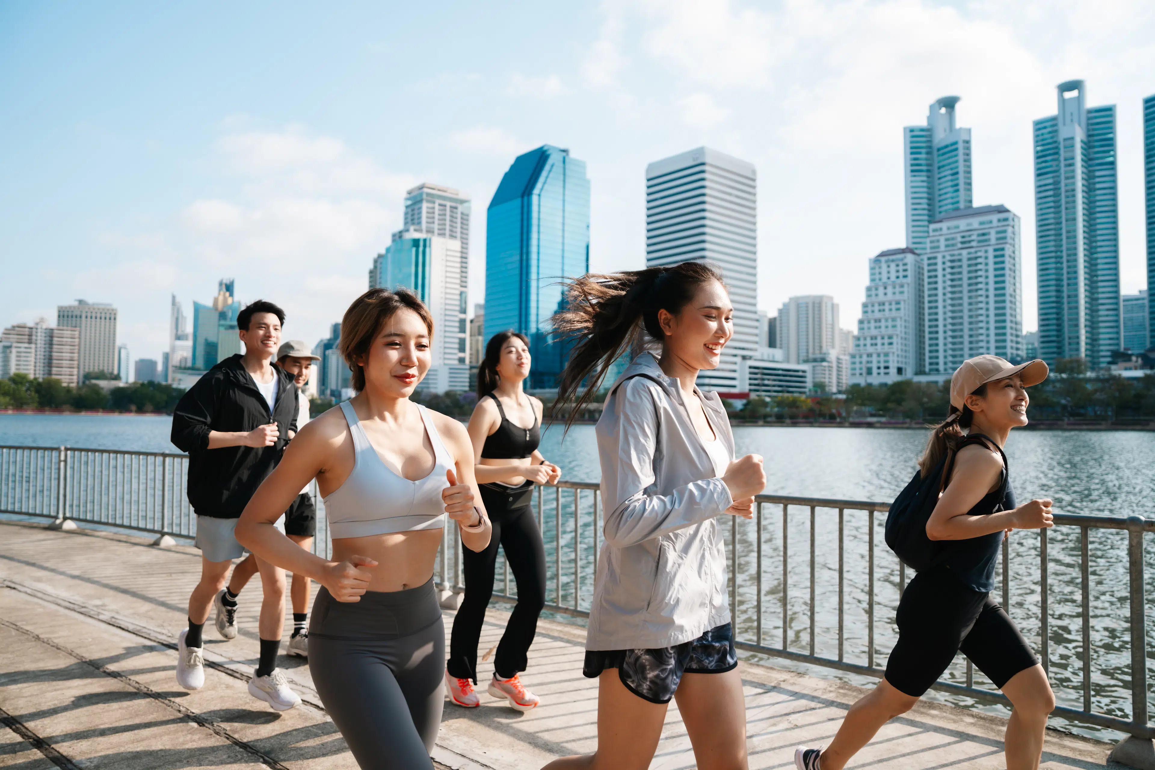 Group of young adults running outside on a waterfront path in a city.