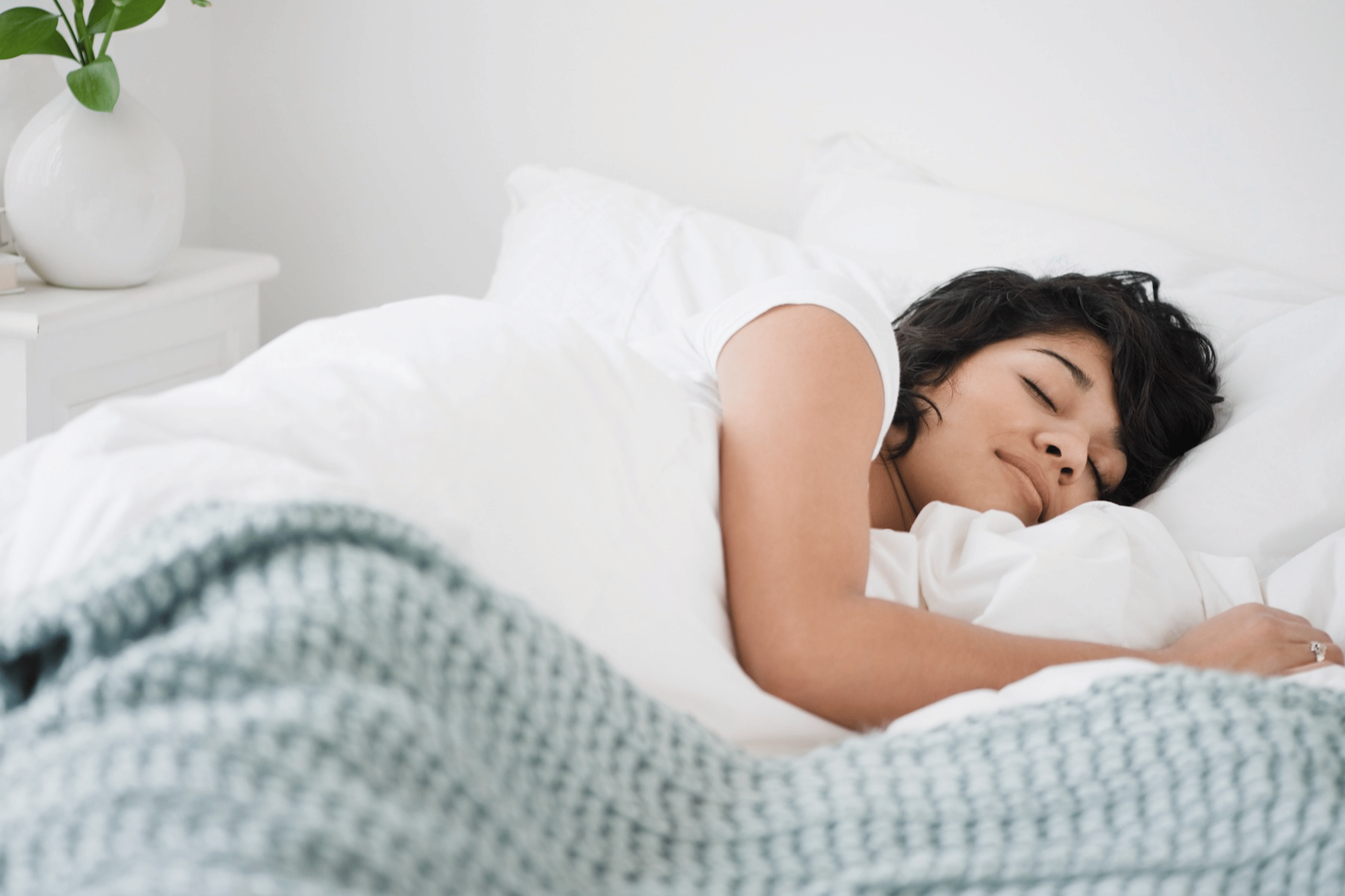 A woman sleeping peacefully in a bright, sunny bedroom. Learn how many hours of REM sleep you need in this article.
