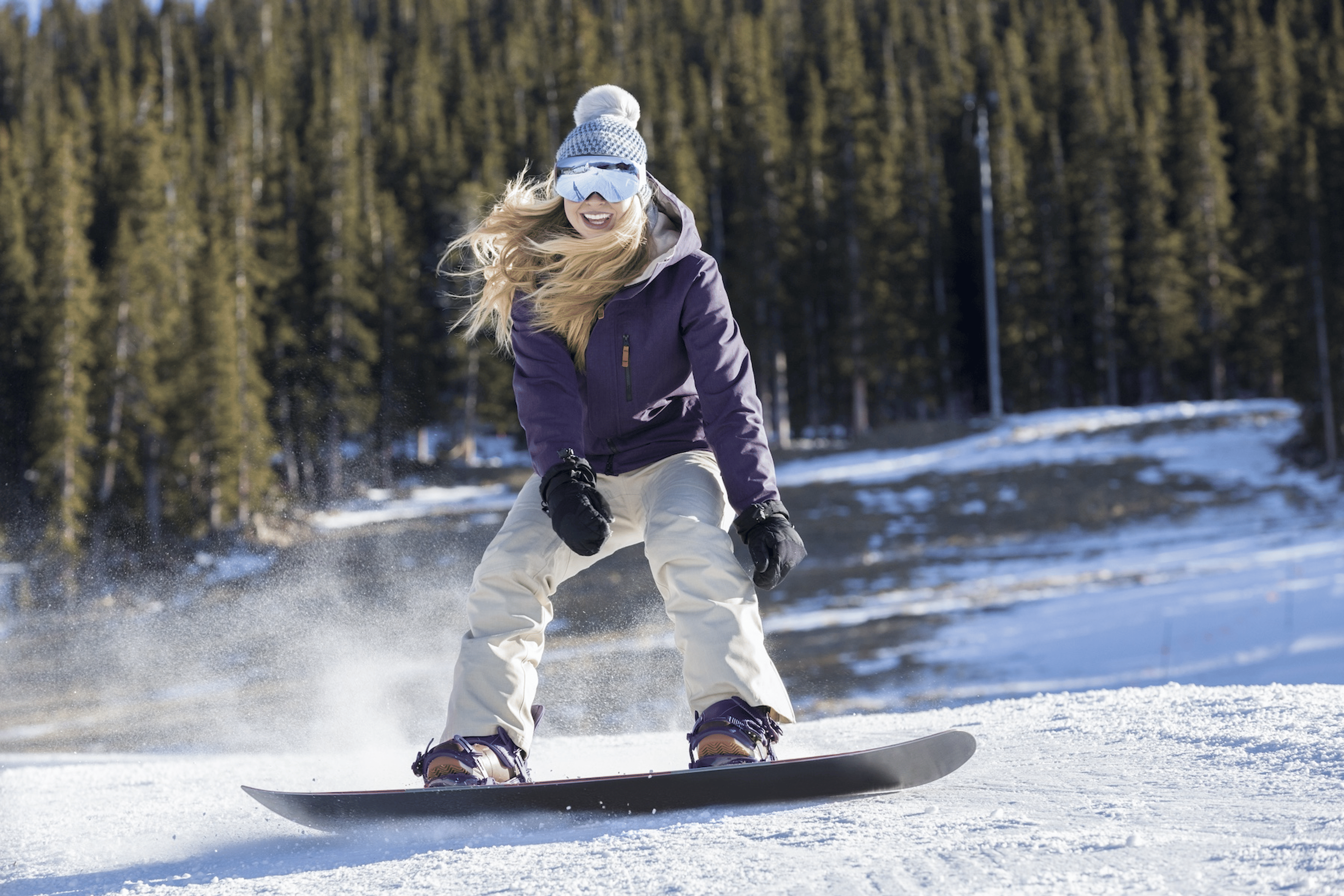 A woman happily trying new things by snowboarding at a mountain resort.