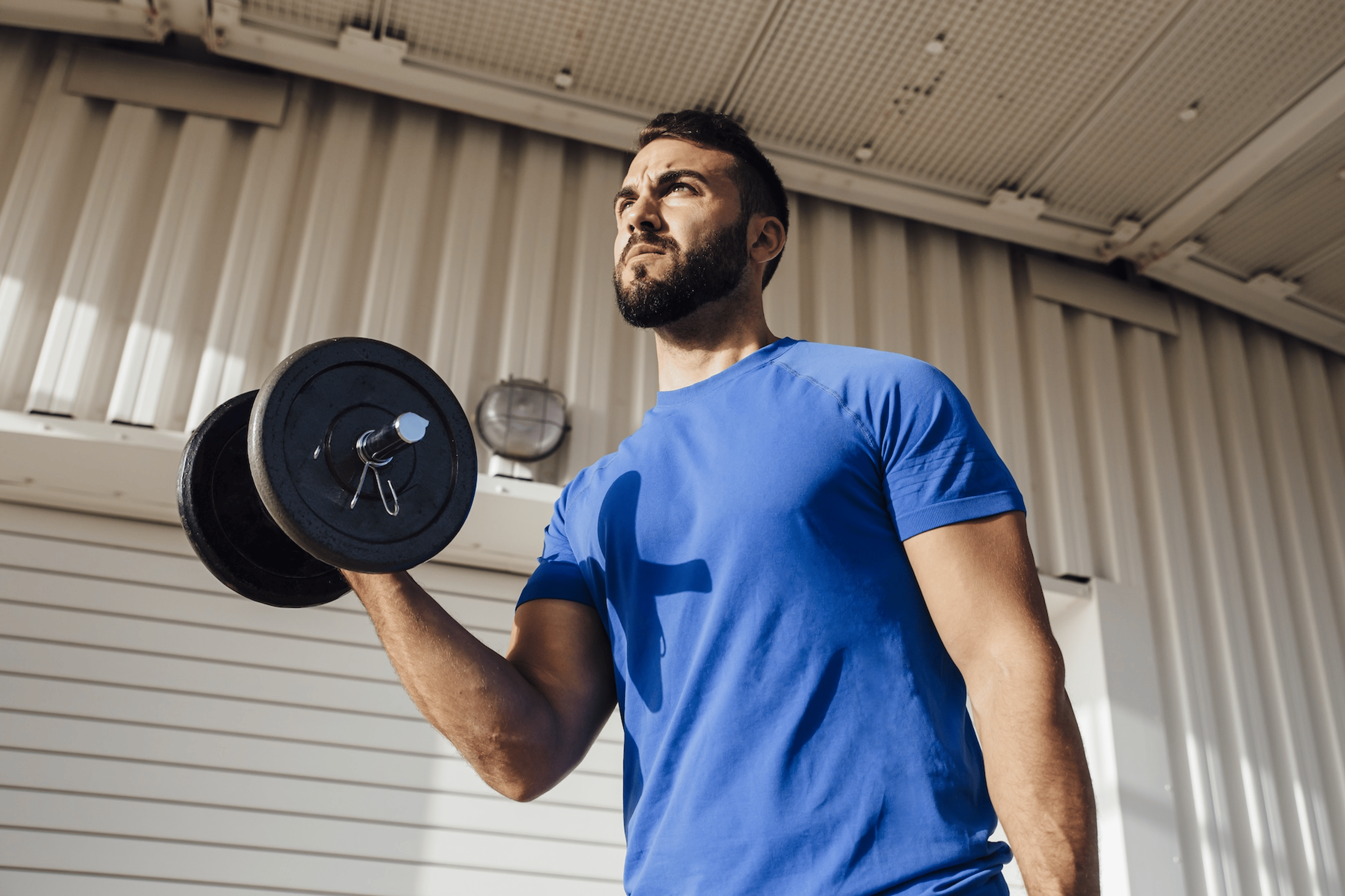 A man lifting a dumbbell while standing near a wall. Learn if working out increases testosterone in this article.