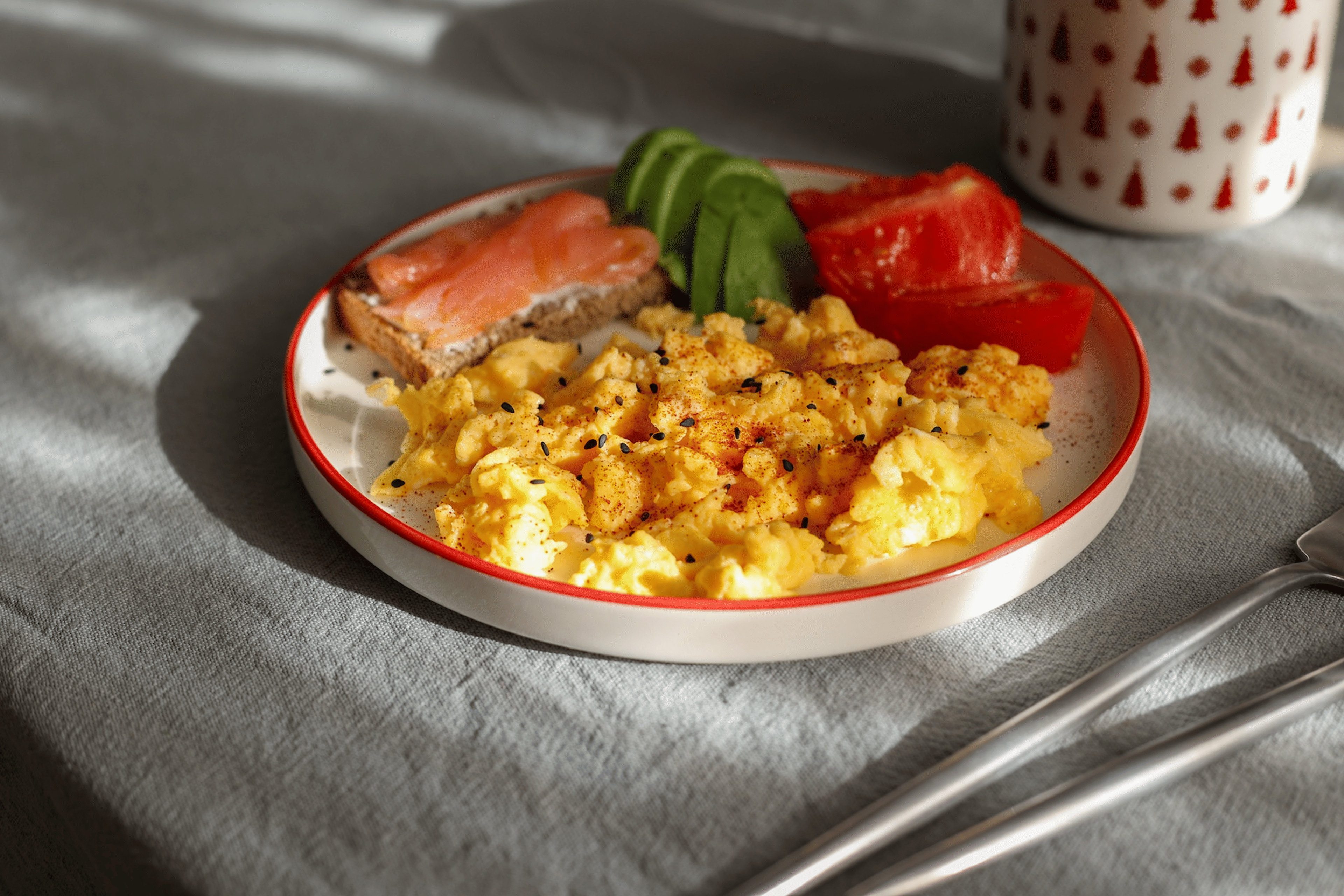A plate with scrambled eggs, avocado, salmon on toast, and tomatoes.