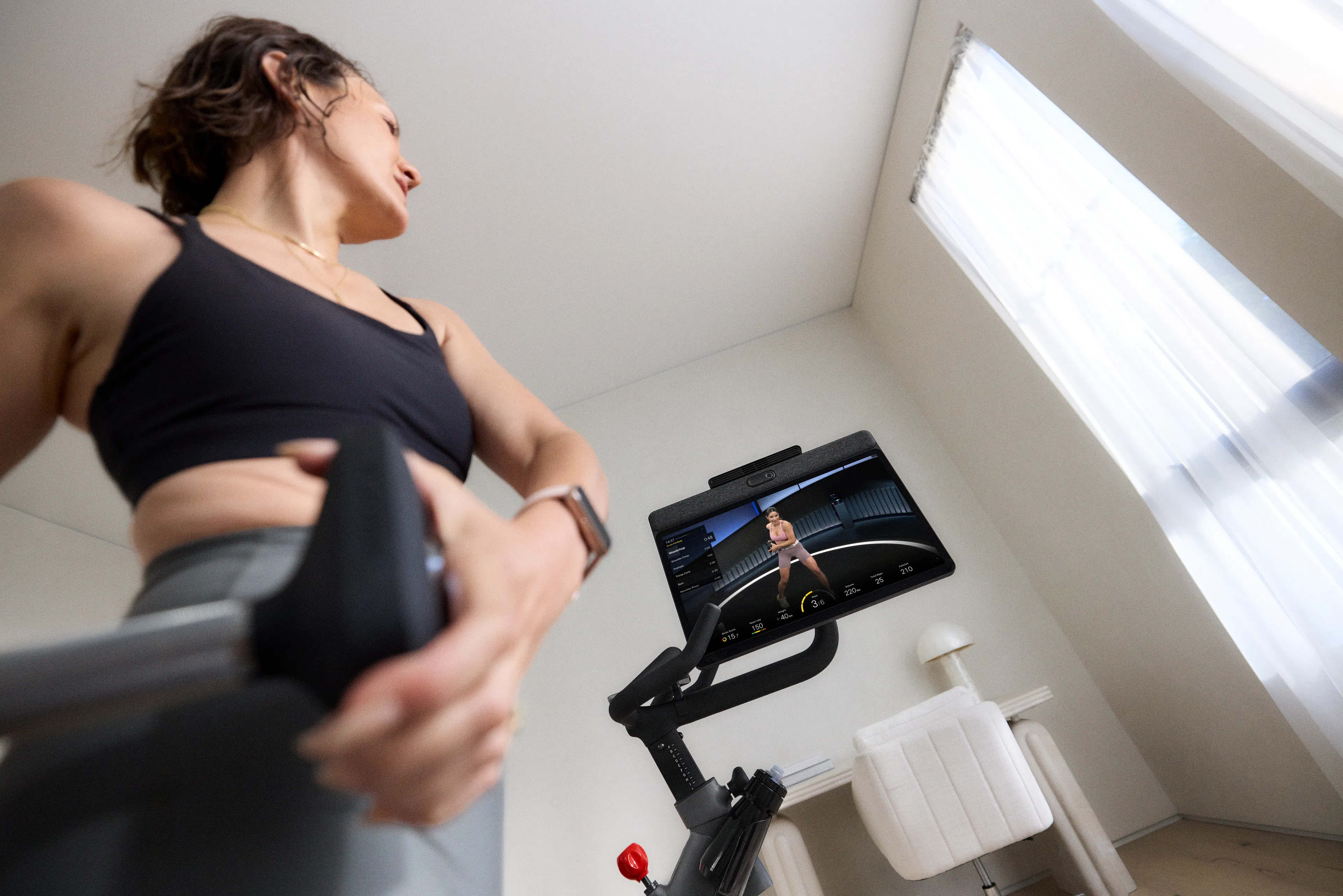 Woman lifts weights during a cross training workout for cycling while standing next to a Peloton Bike+.