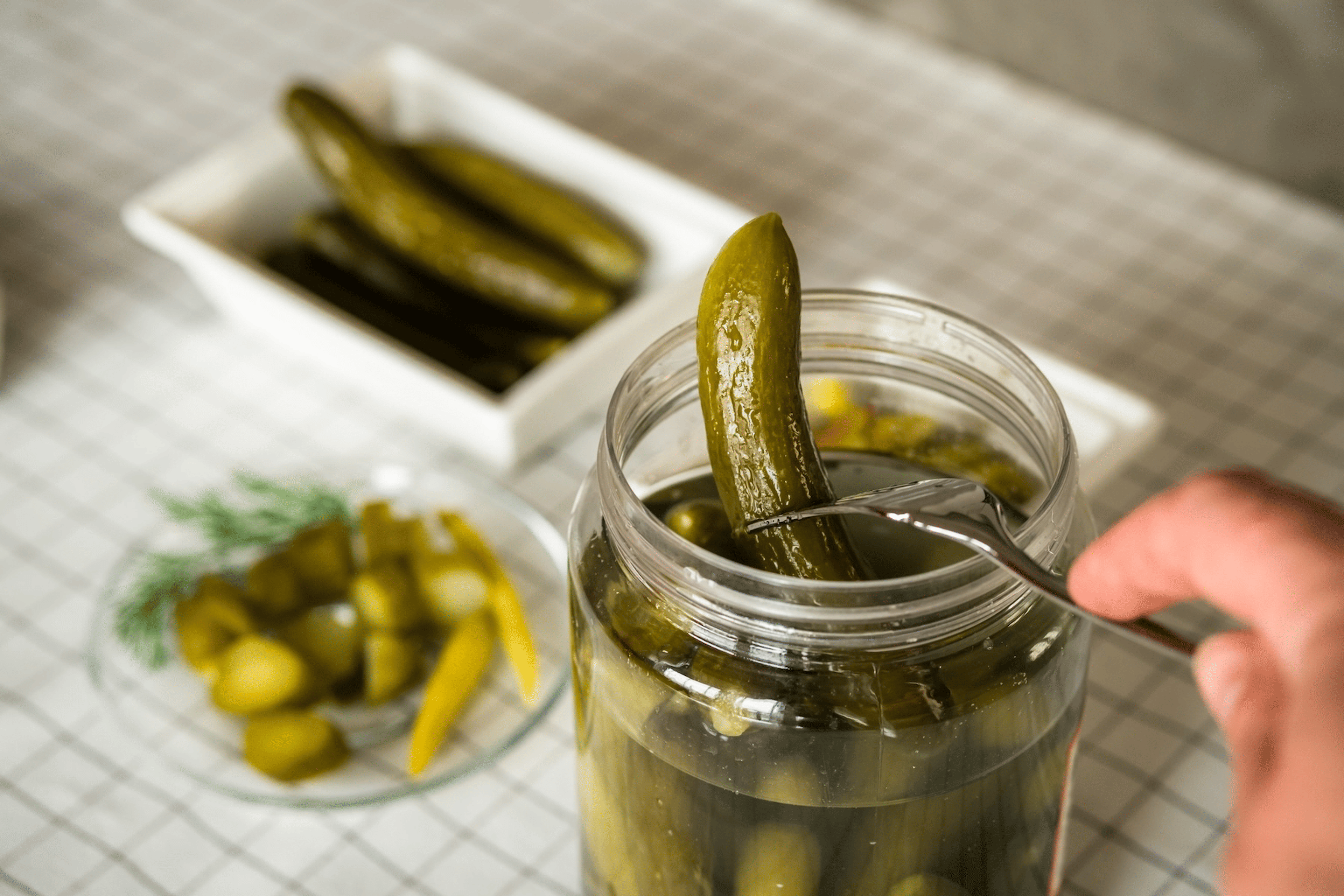A close-up photo of someone using a fork to take a pickle out of a pickle jar.