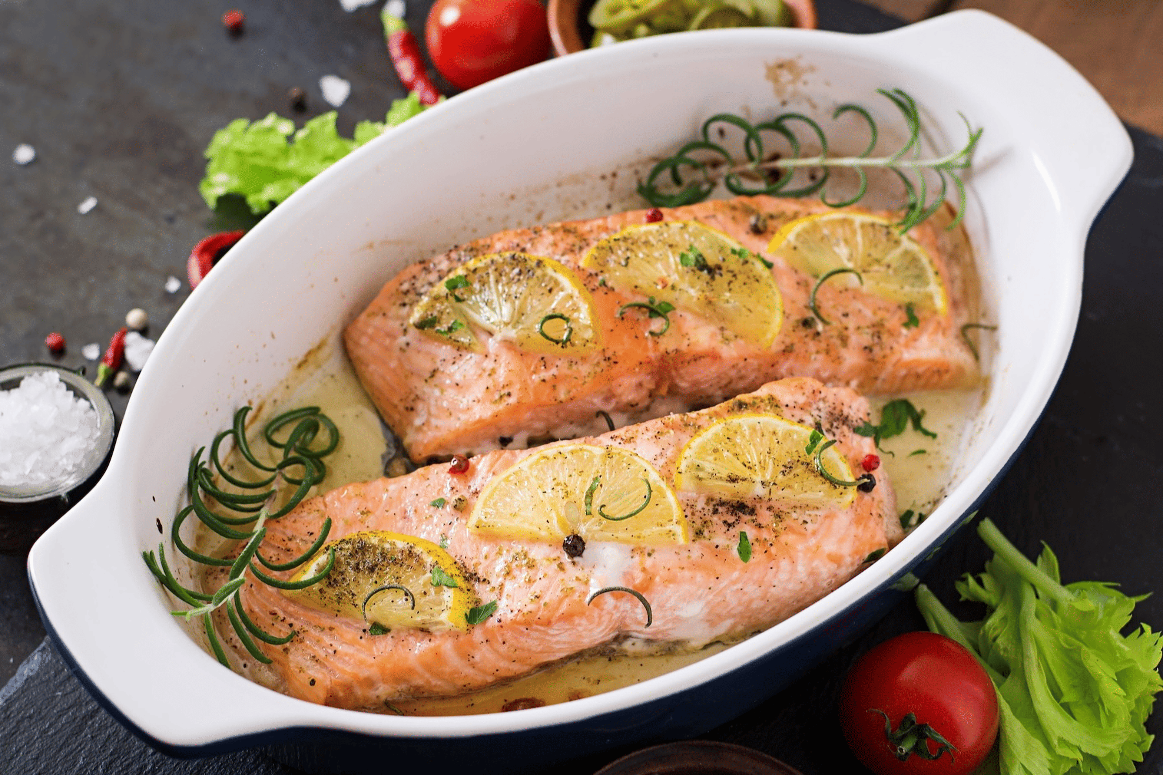 A small baking dish with two cooked salmon fillets garnished with lemon and rosemary.