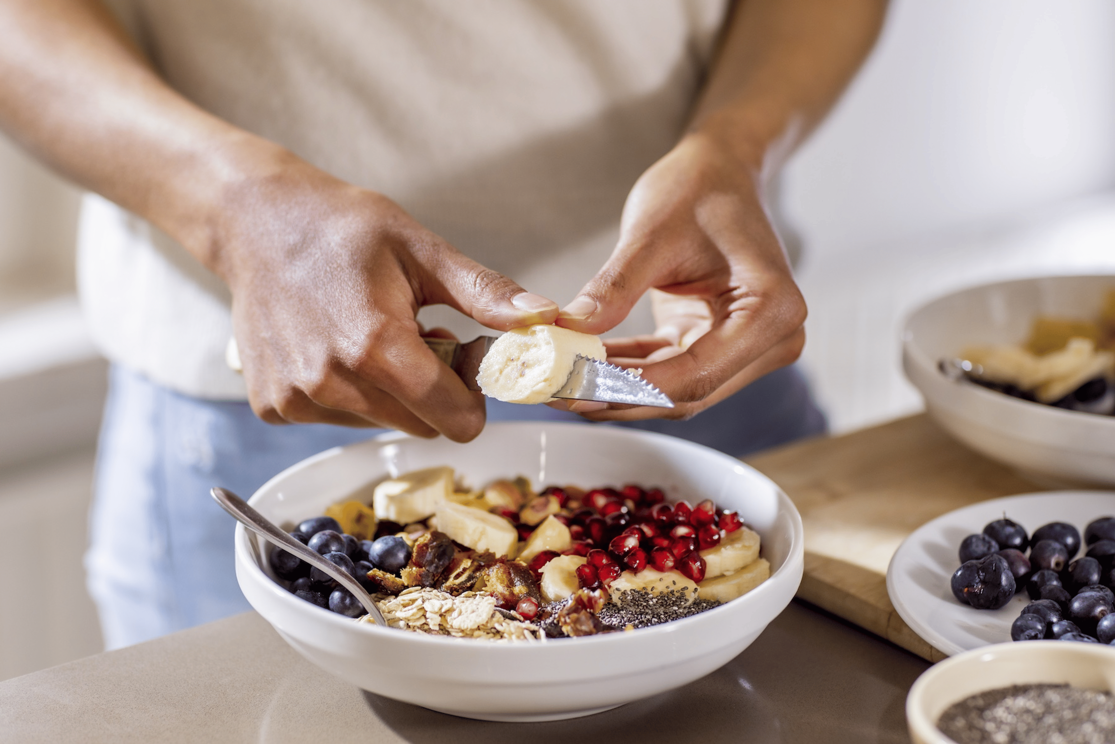 A close-up photo of a woman slicing banana (a muscle recovery food) into her yogurt and oats bowl.