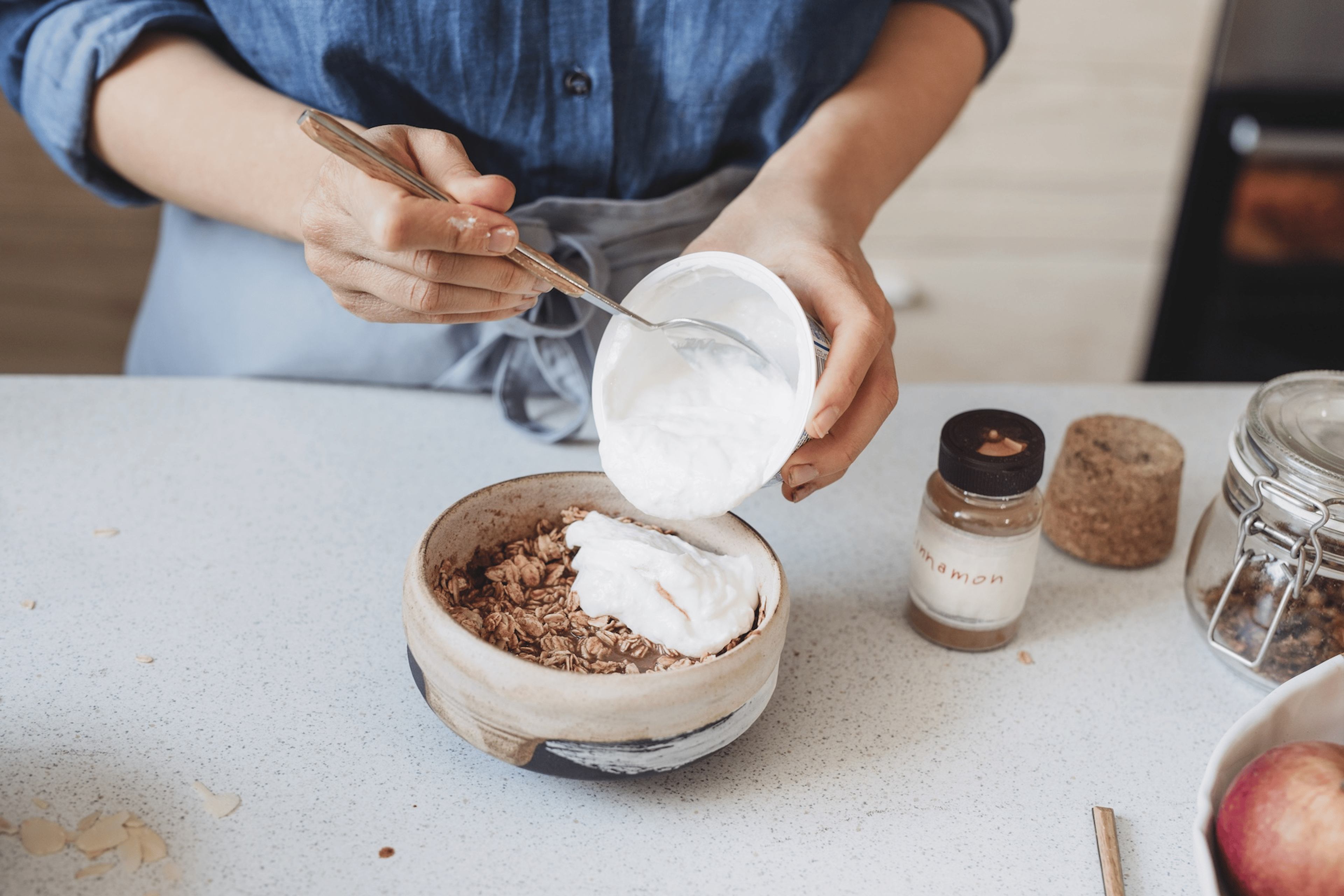 A woman adding Greek yogurt to her overnight oats in order to get more protein.
