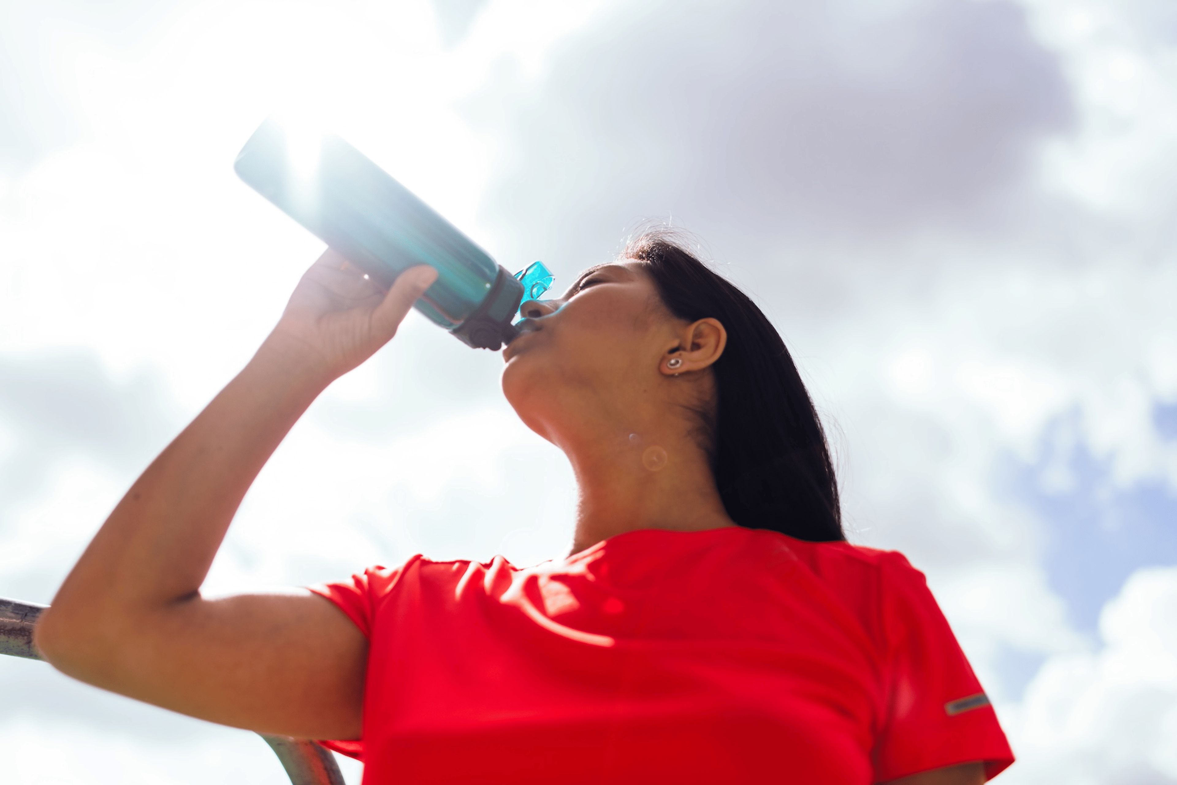 An athlete in a red shirt drinking from a water bottle on a sunny day.