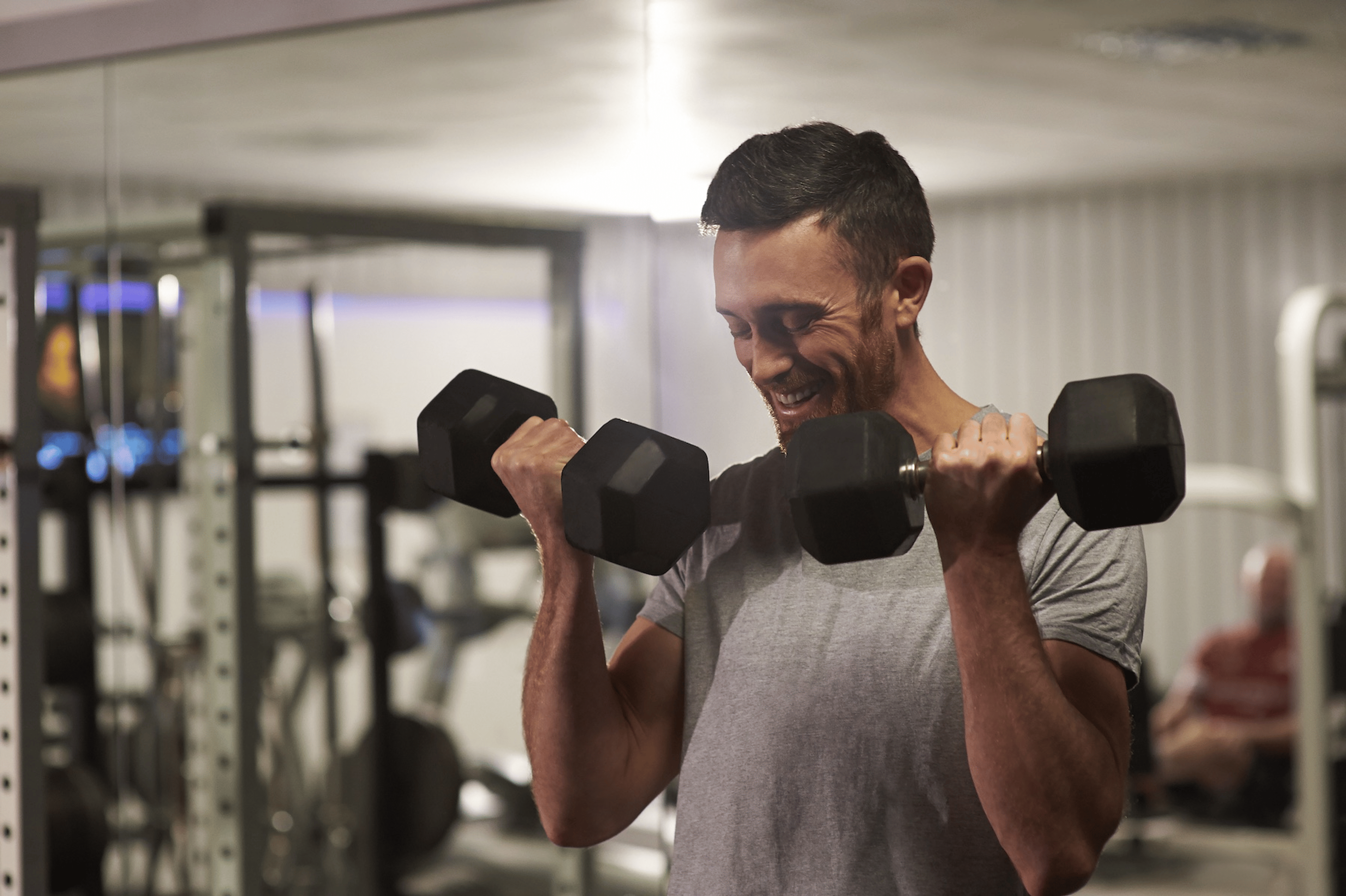 A man happily lifting dumbbells in a bicep curl at a gym.