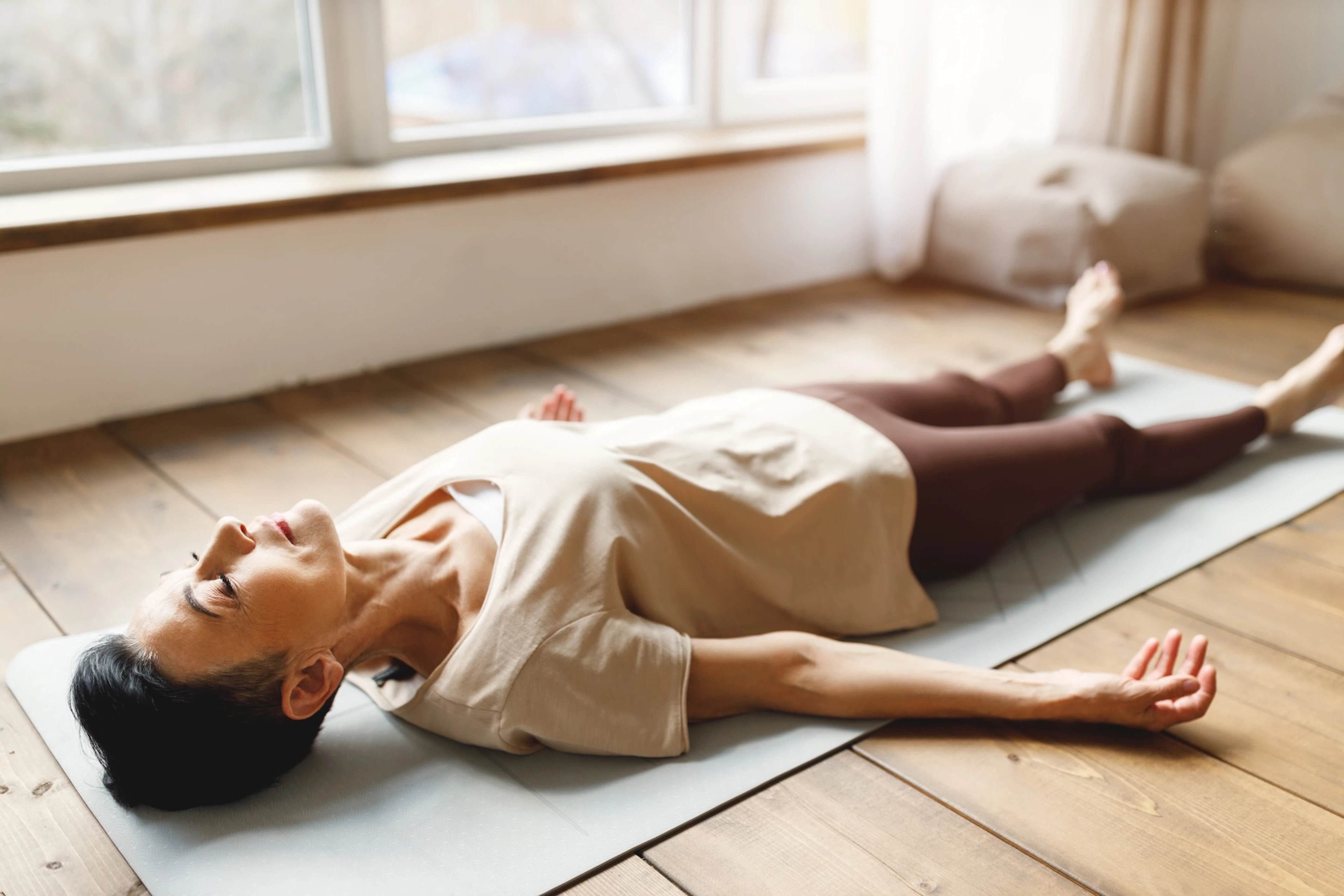 A woman in Savasana pose on her yoga mat at home.