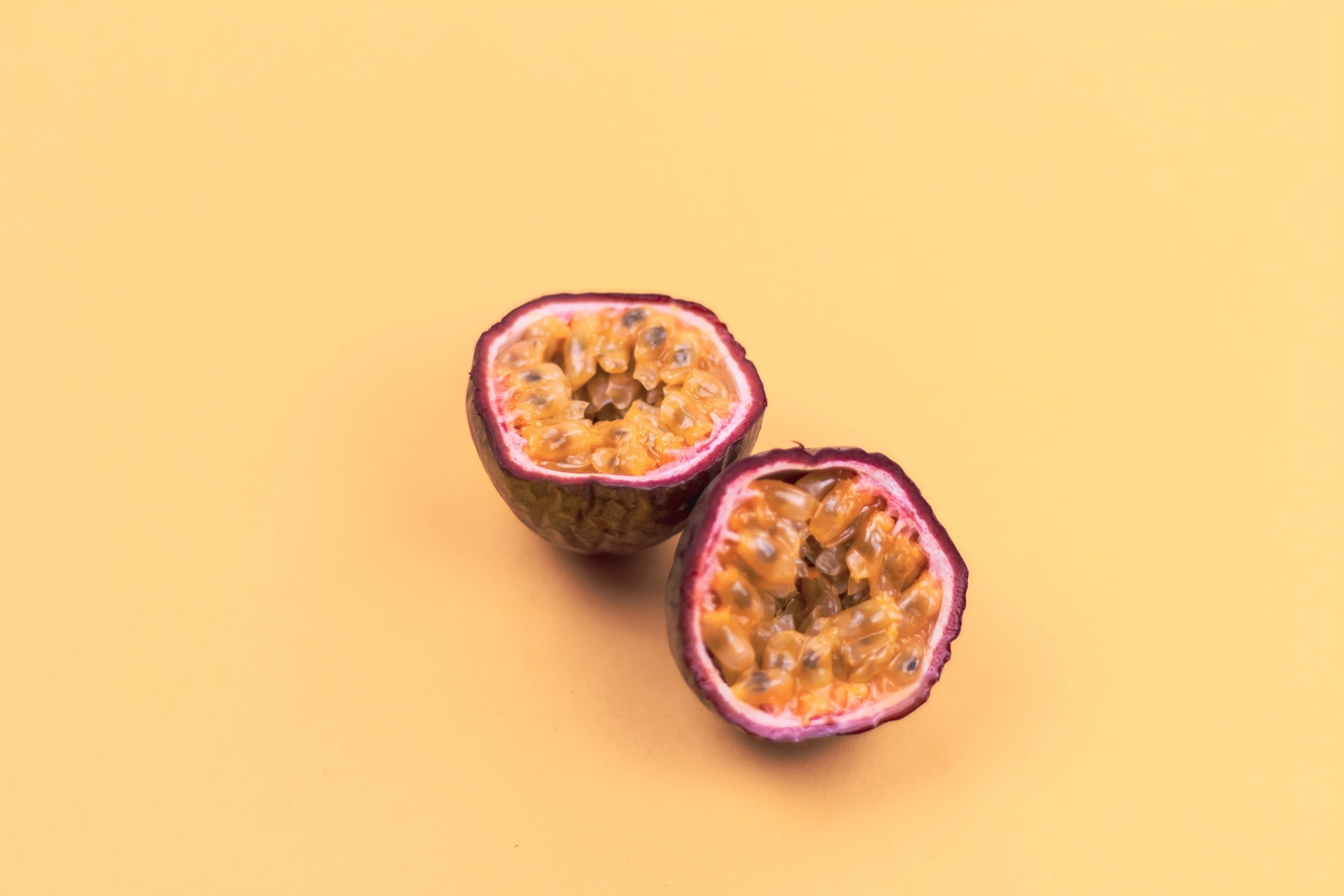 A passion fruit cut in half, resting on a yellow backgorund.