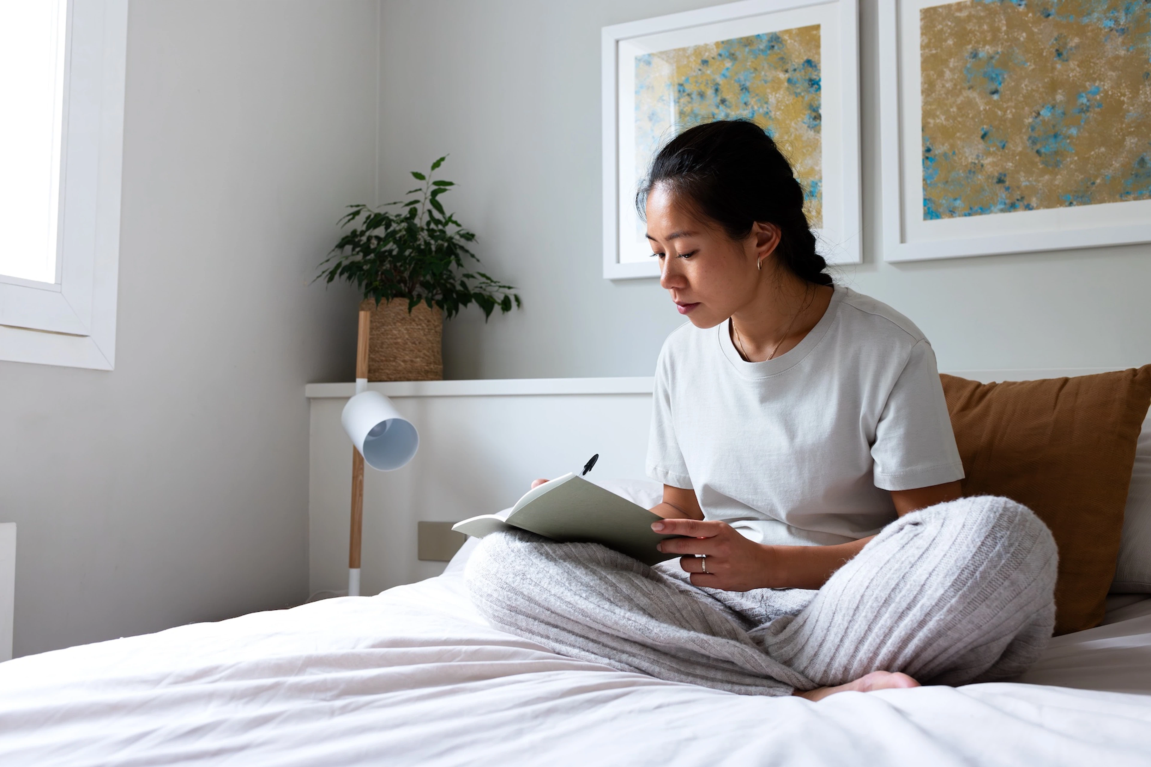 A woman journaling about her goals while sitting on her bed.