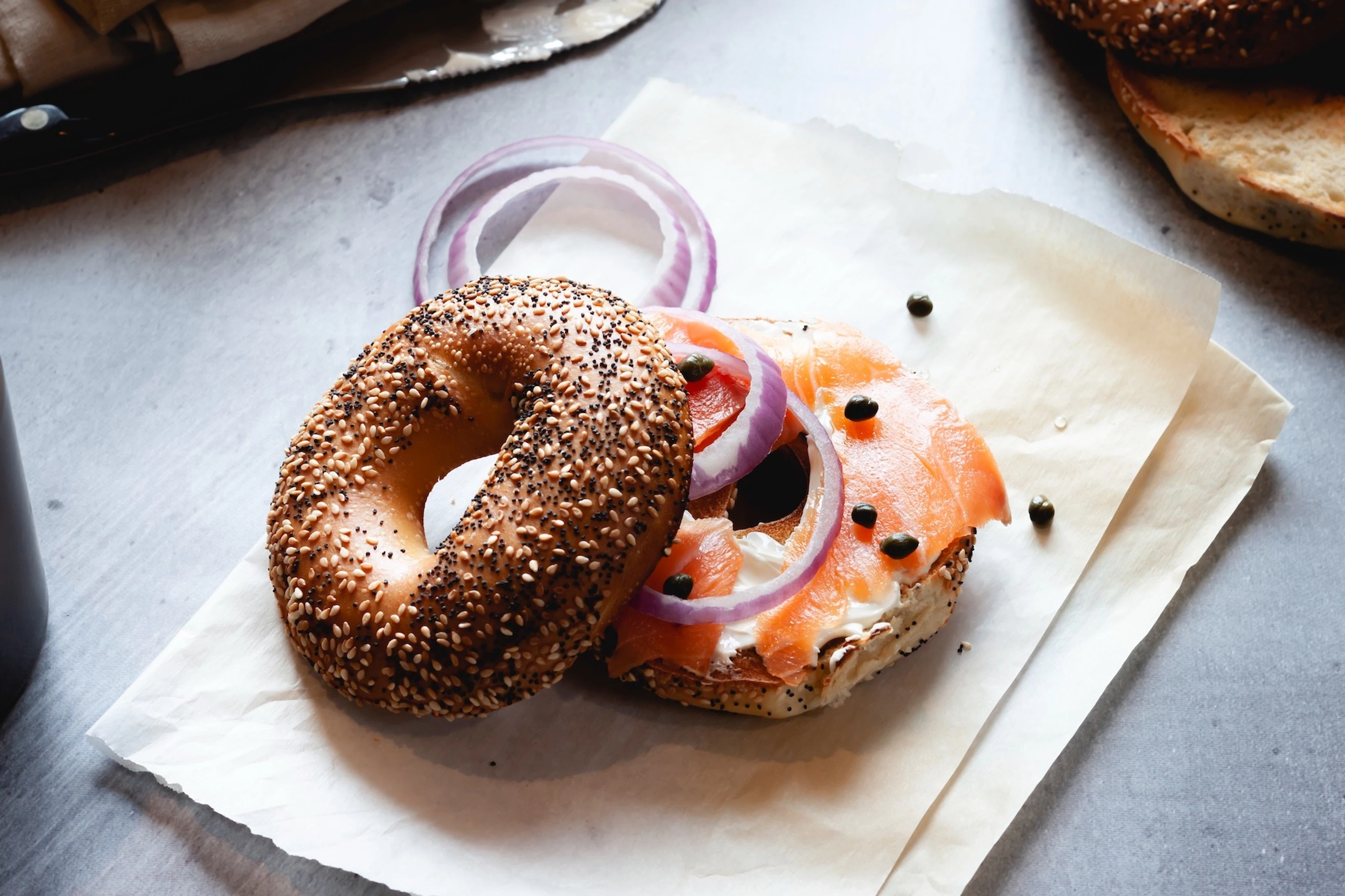 An everything bagel with cream cheese, salmon, red onions, and capers resting on a brown parchment bag.
