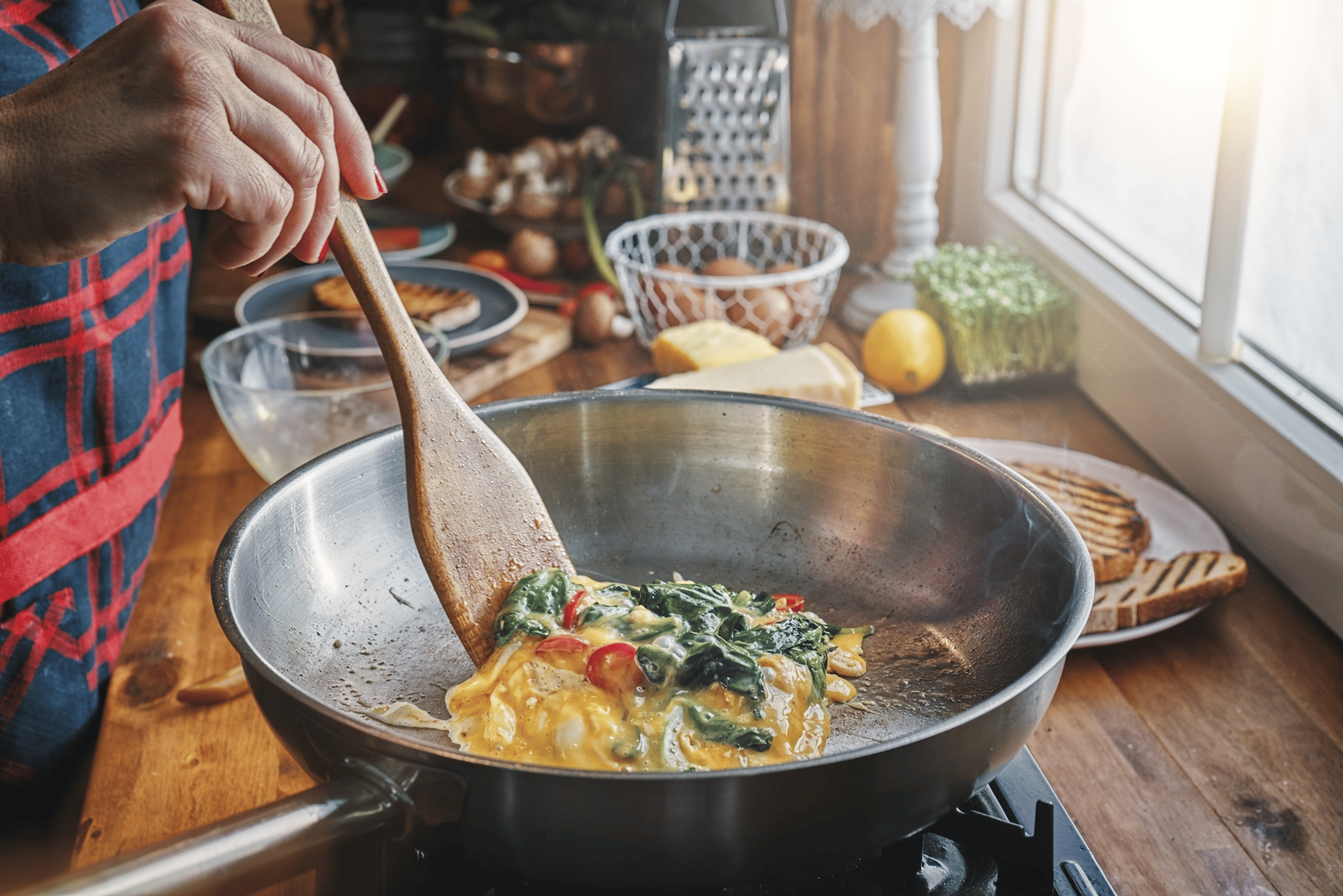 Close-up photo of someone following a healthy habit by making an egg omelet with tomatoes and spinach.