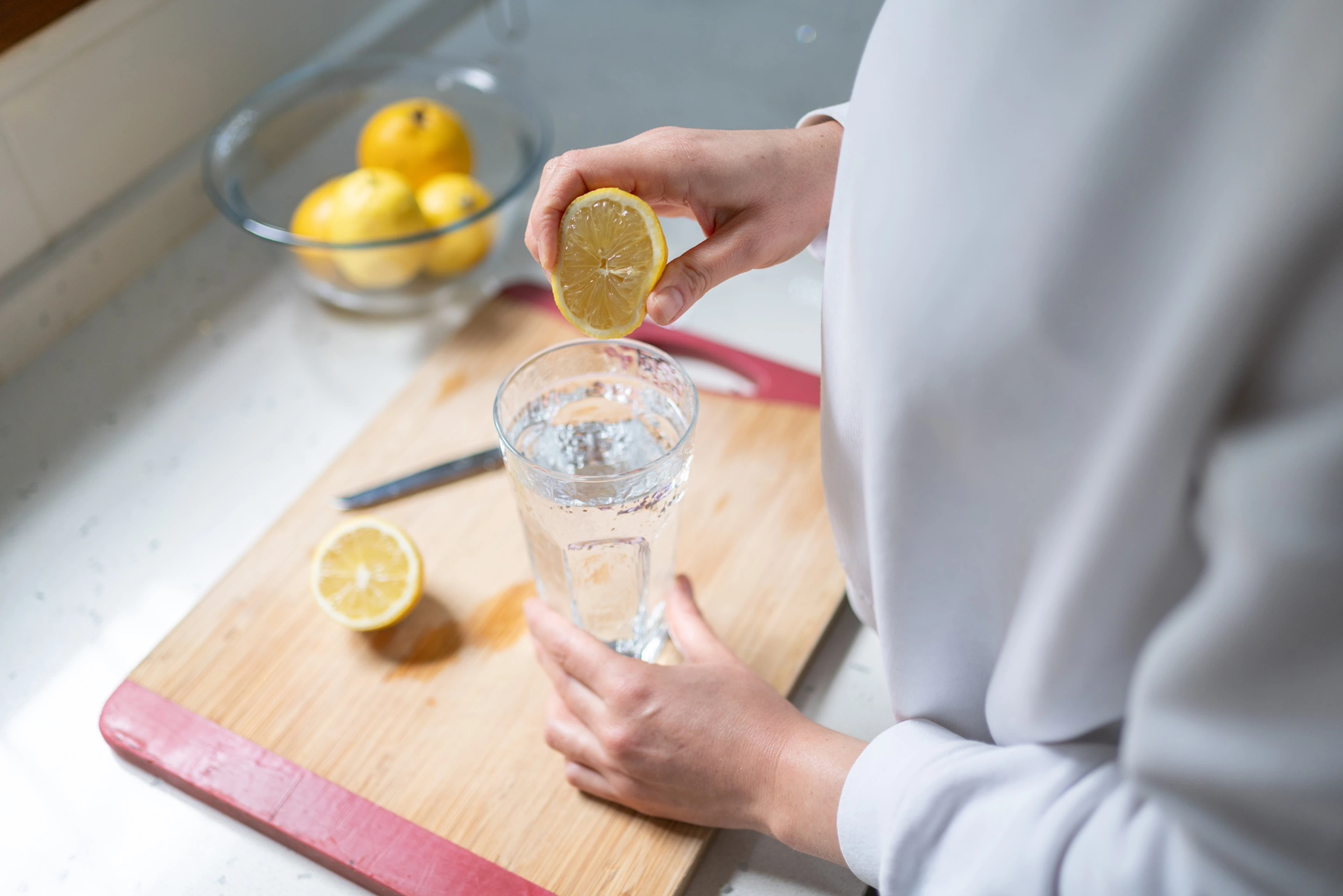 A person squeezing lemon into a glass of water to help them stay hydrated.